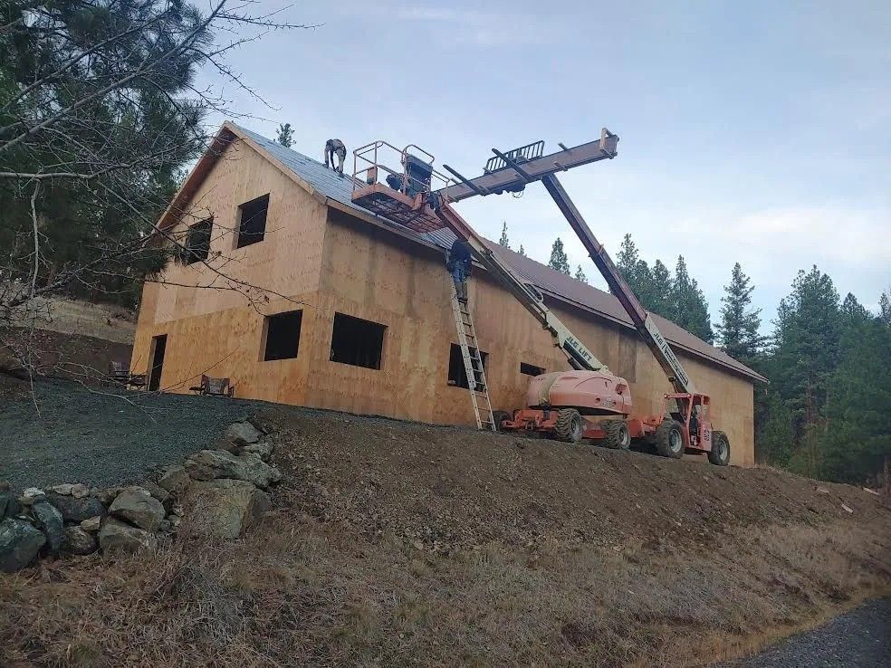 House under construction with workers on a roof and lift on a wooded hillside