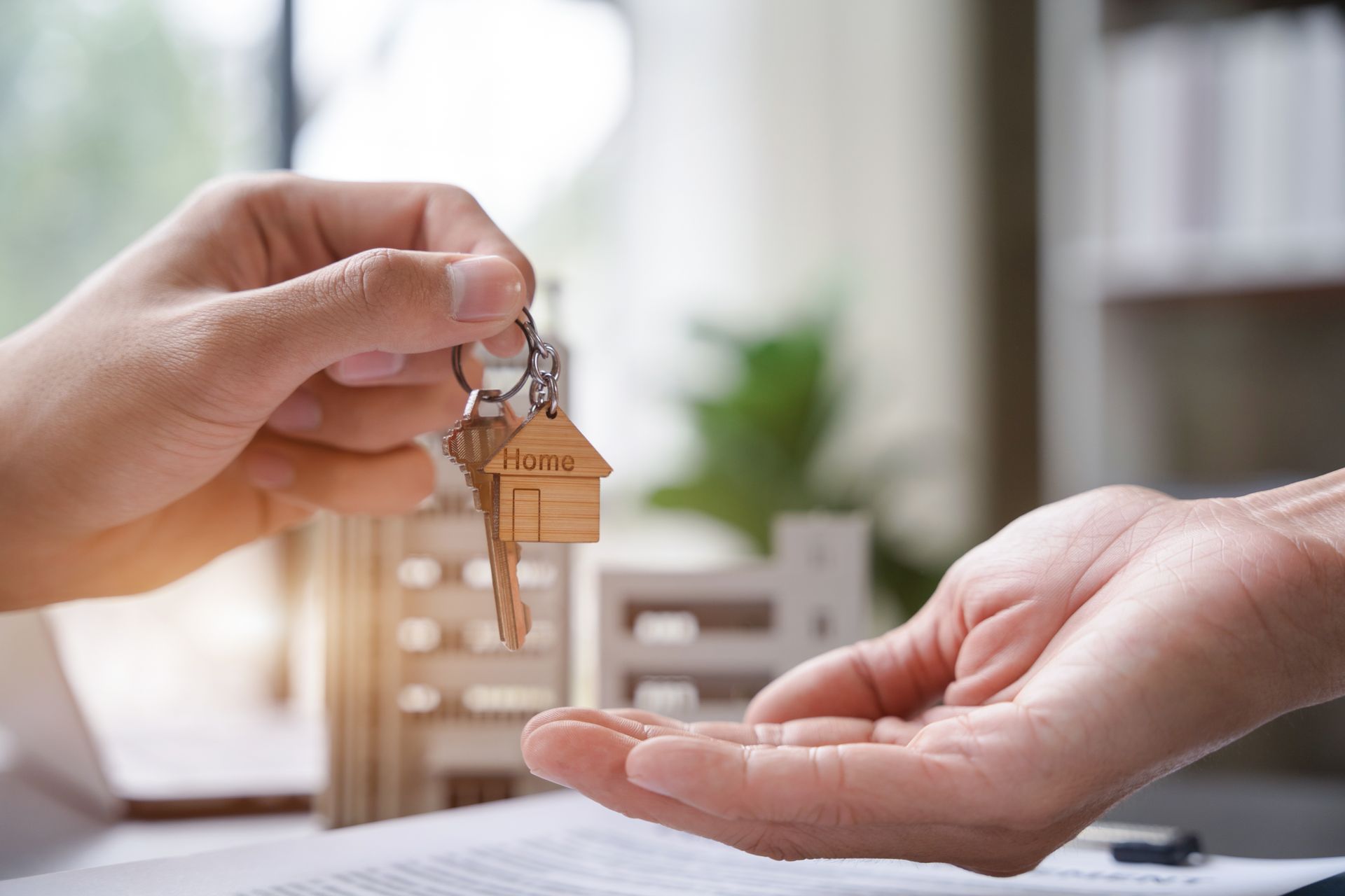 Hands exchanging a small house keychain over an open palm in a bright home setting