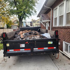 A dumpster full of junk is parked in front of a brick house