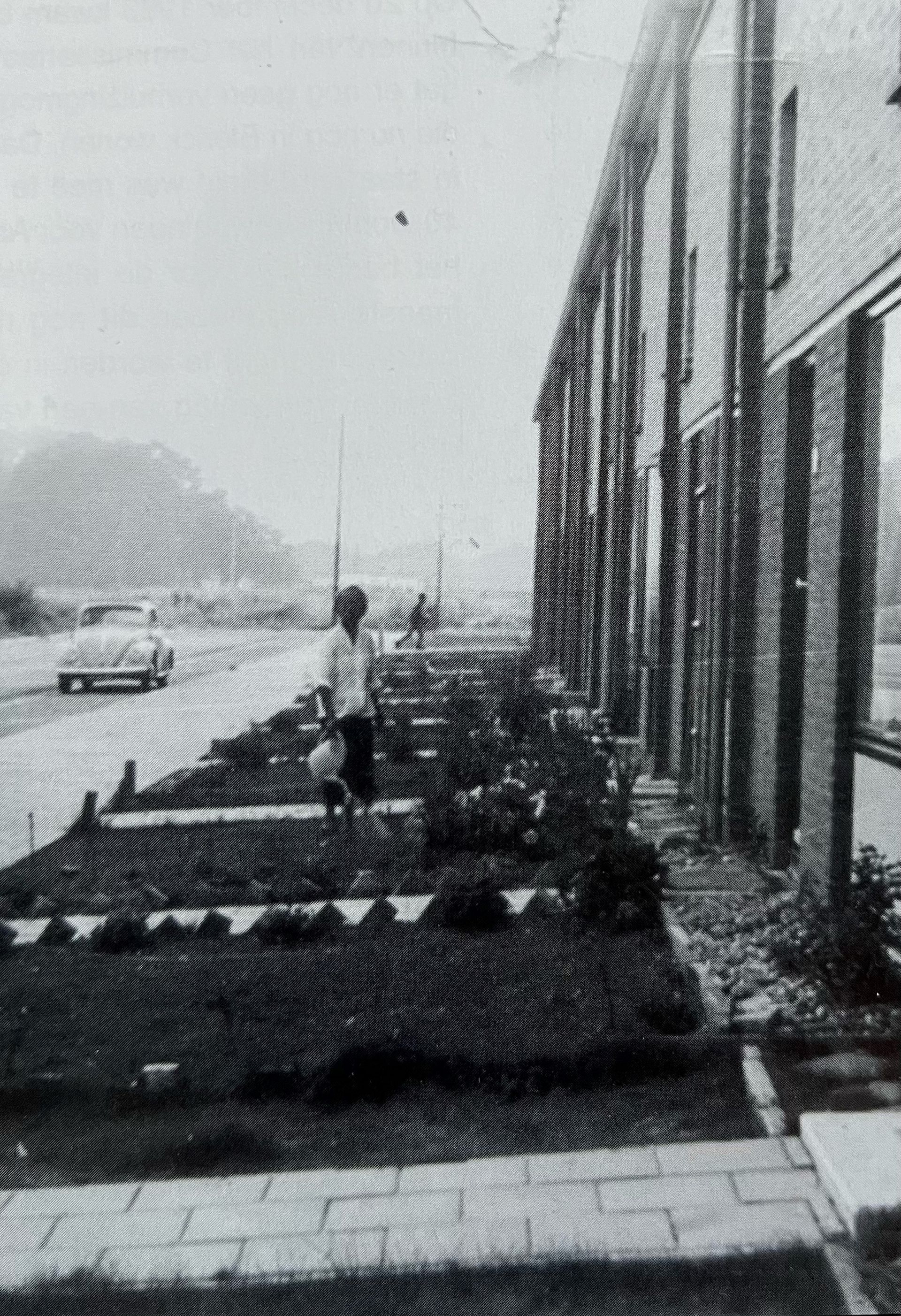 Een zwart-witfoto van een vrouw die over het trottoir voor een gebouw loopt.