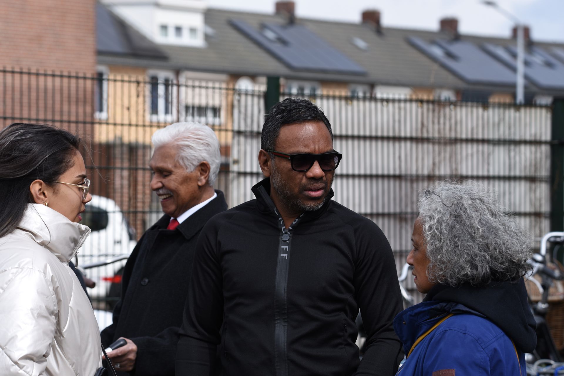 Een groep mensen staat voor een hek met elkaar te praten.