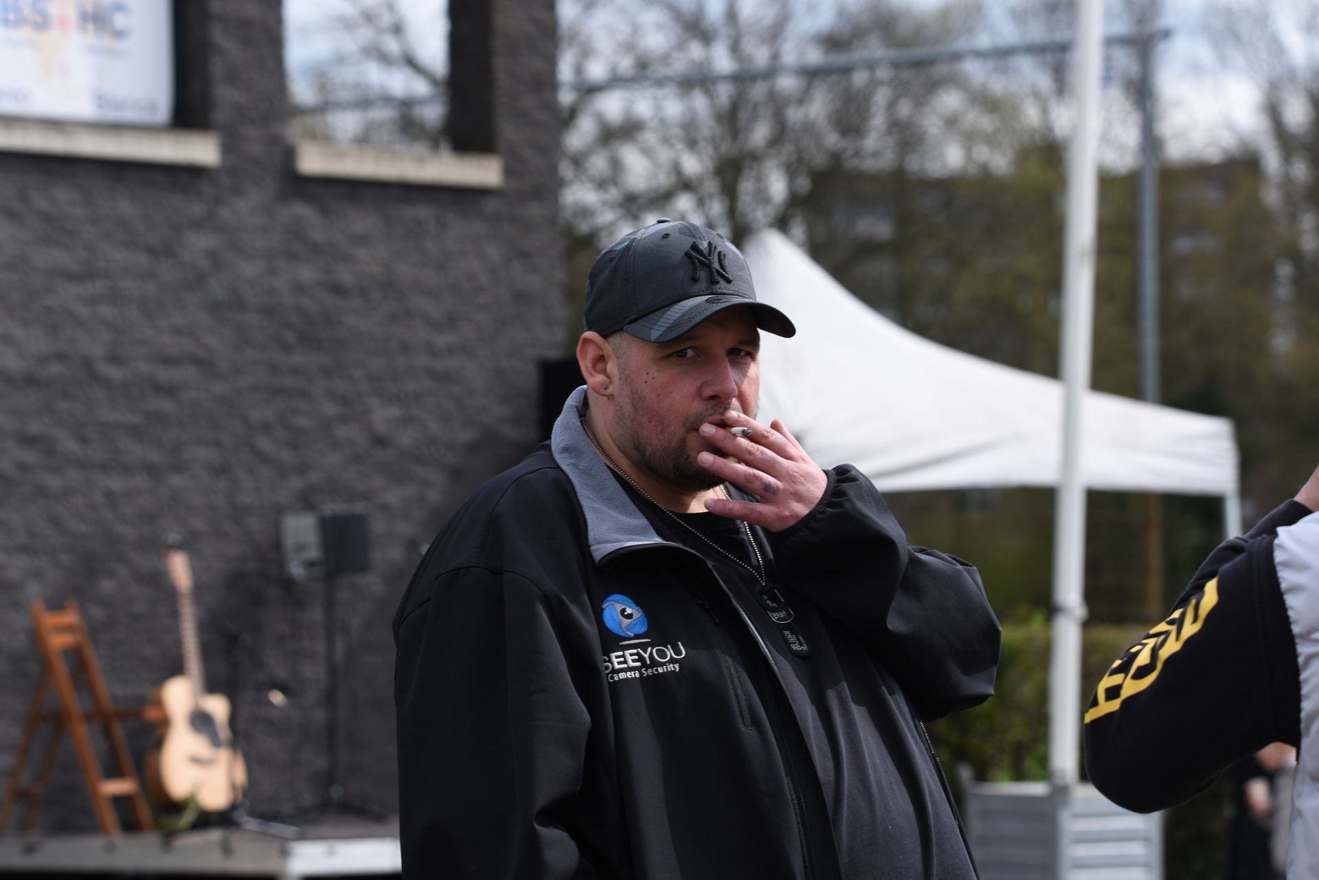 Een man in een zwart jasje en hoed bedekt zijn mond met zijn hand.