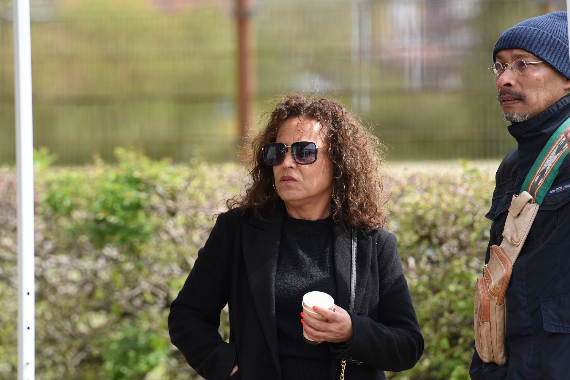 Een man en een vrouw staan ​​naast elkaar. de vrouw draagt ​​een zonnebril en houdt een kopje koffie vast.