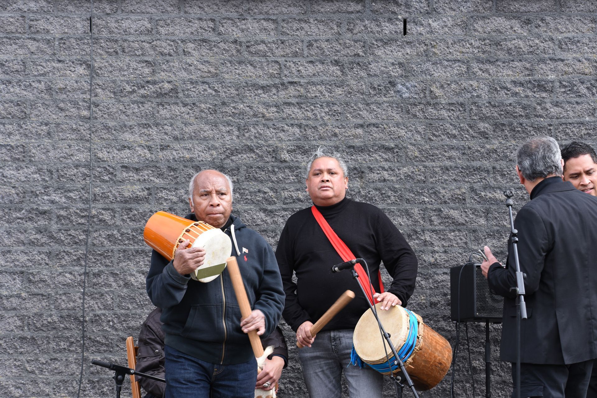 Een groep mannen speelt drums voor een bakstenen muur.