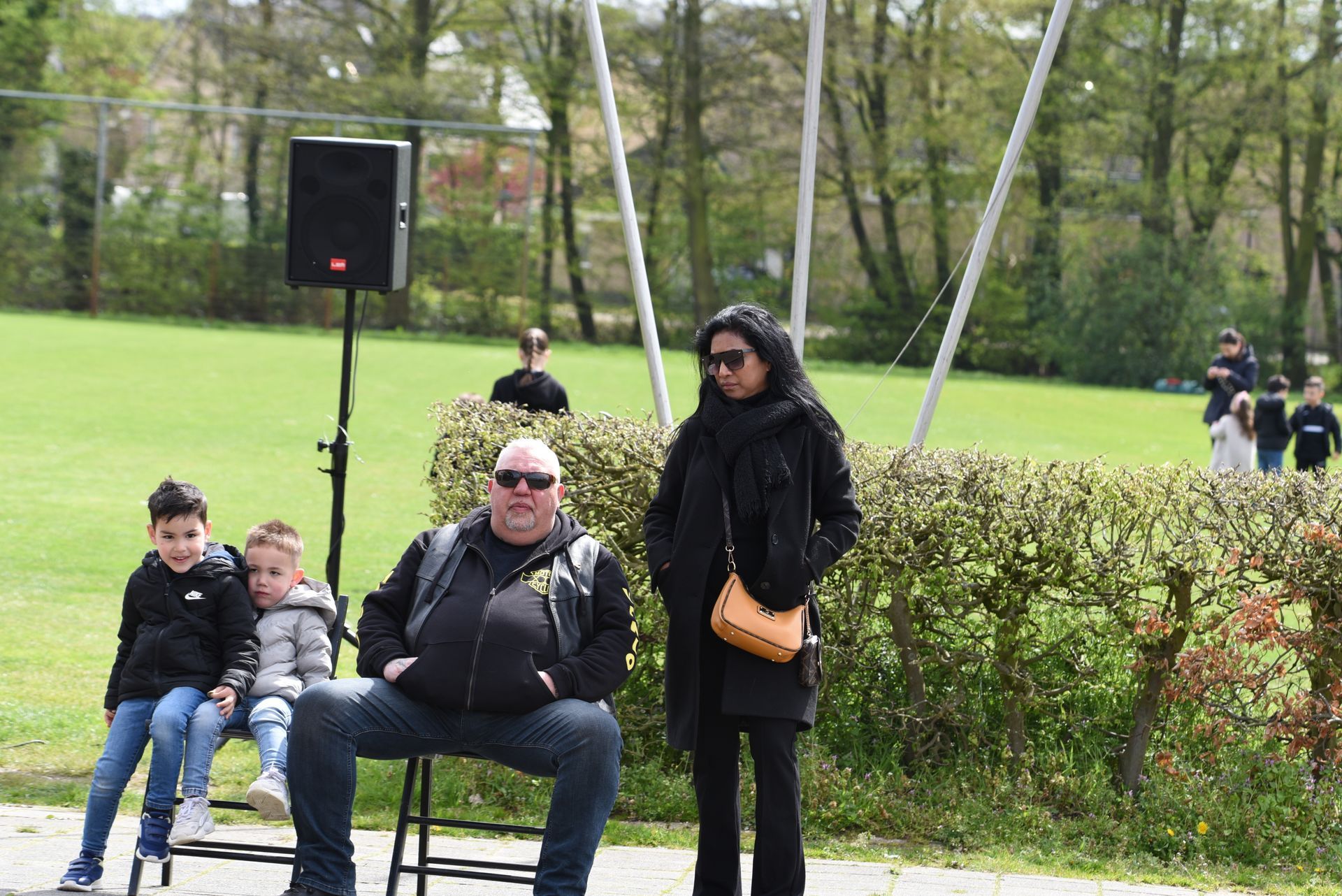 Een man zit met twee kinderen op een krukje in een park.