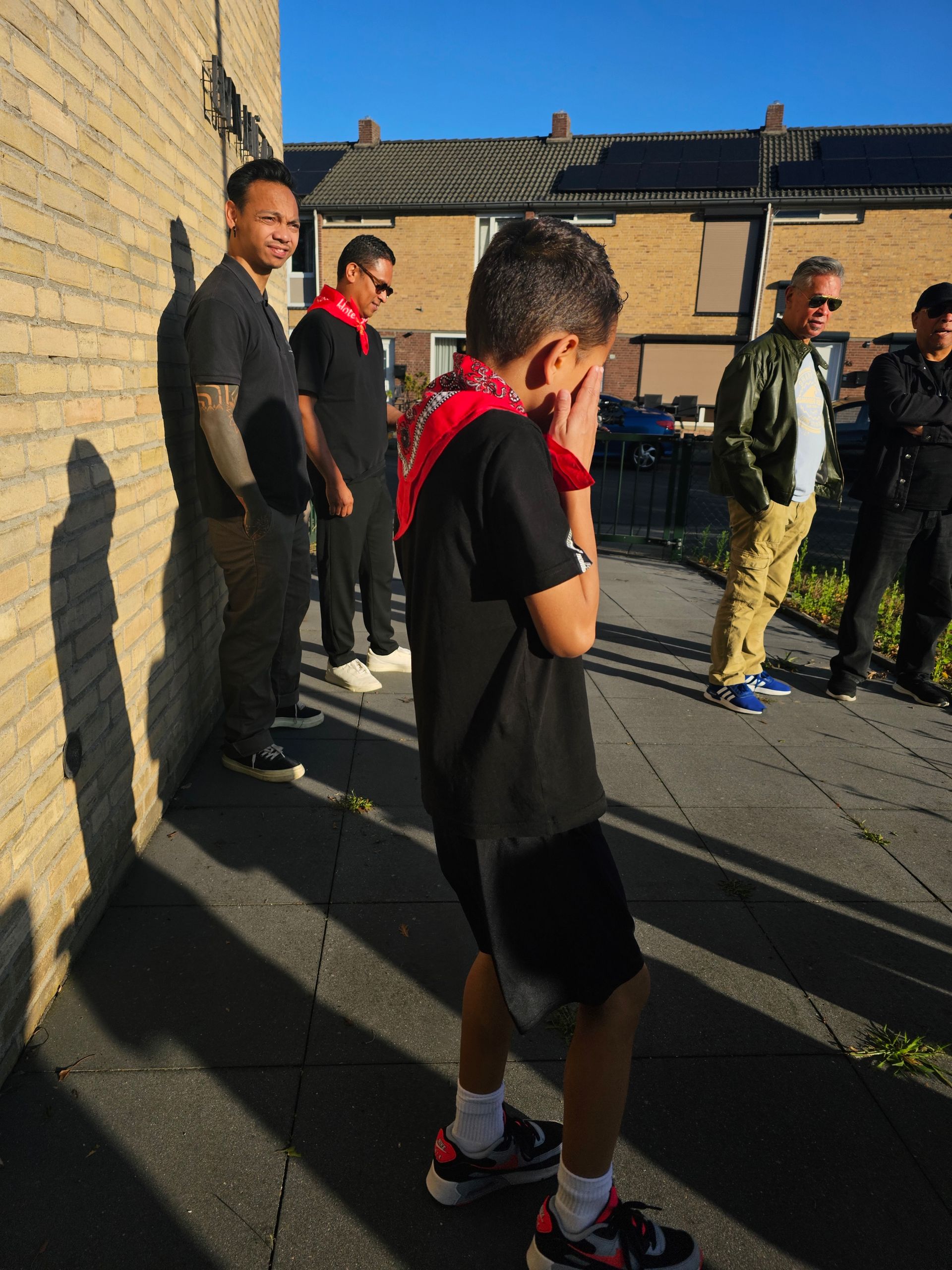 Een jongen met een rode bandana die zijn gezicht bedekt, staat voor een groep mannen