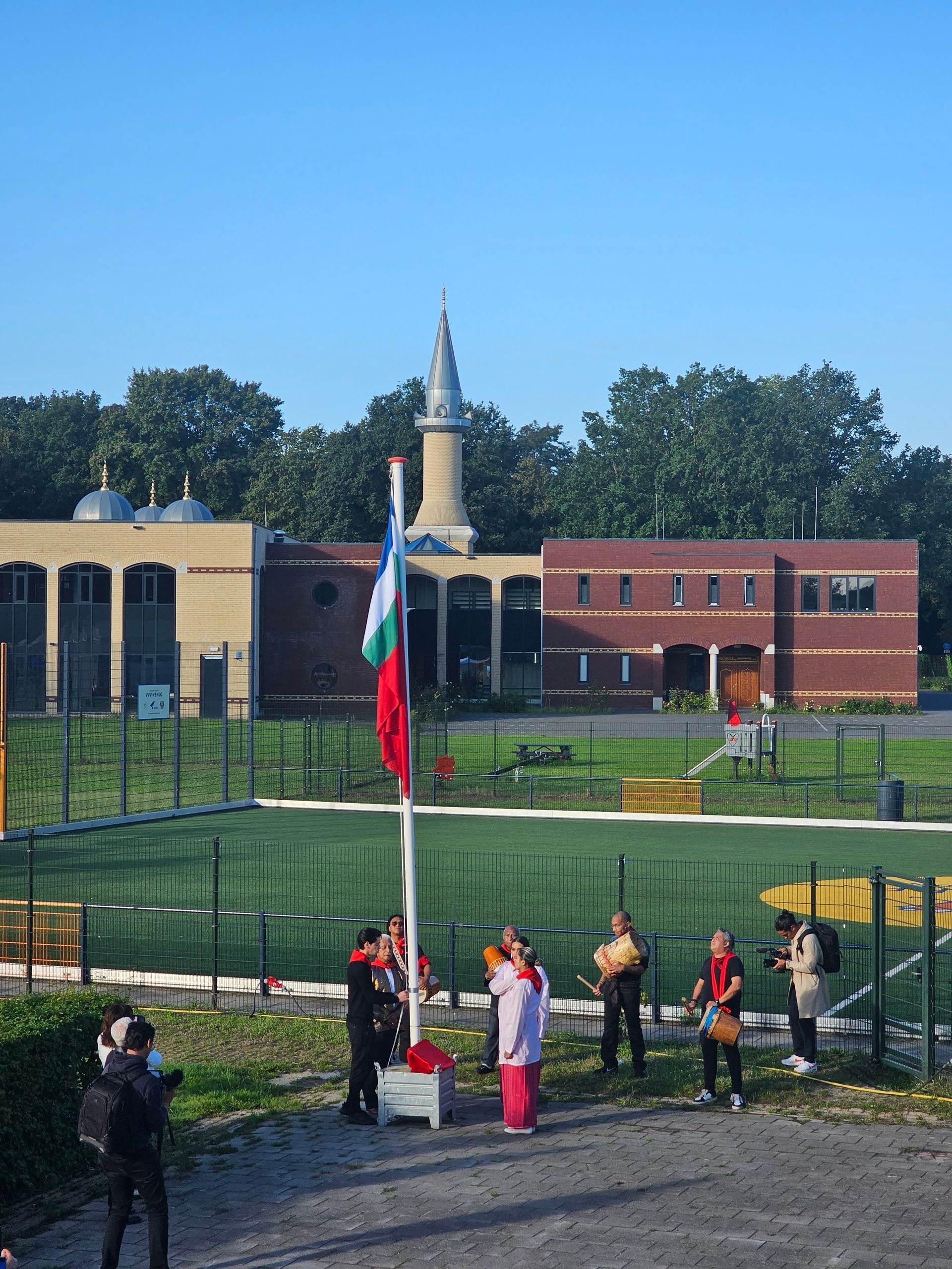 Een groep mensen staan ​​rond een vlaggenmast met een moskee op de achtergrond