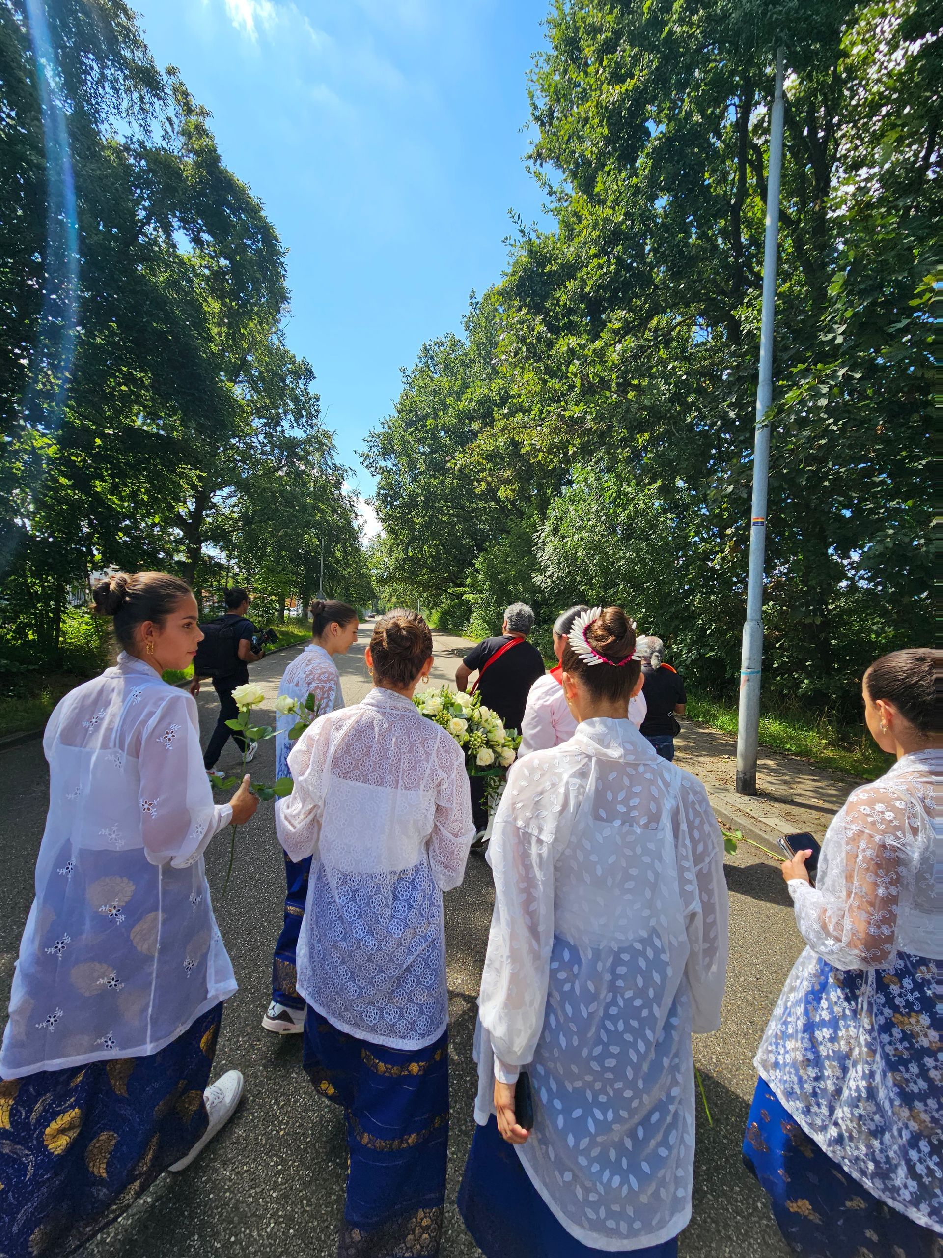Een groep vrouwen loopt over een pad met bloemen in de hand.