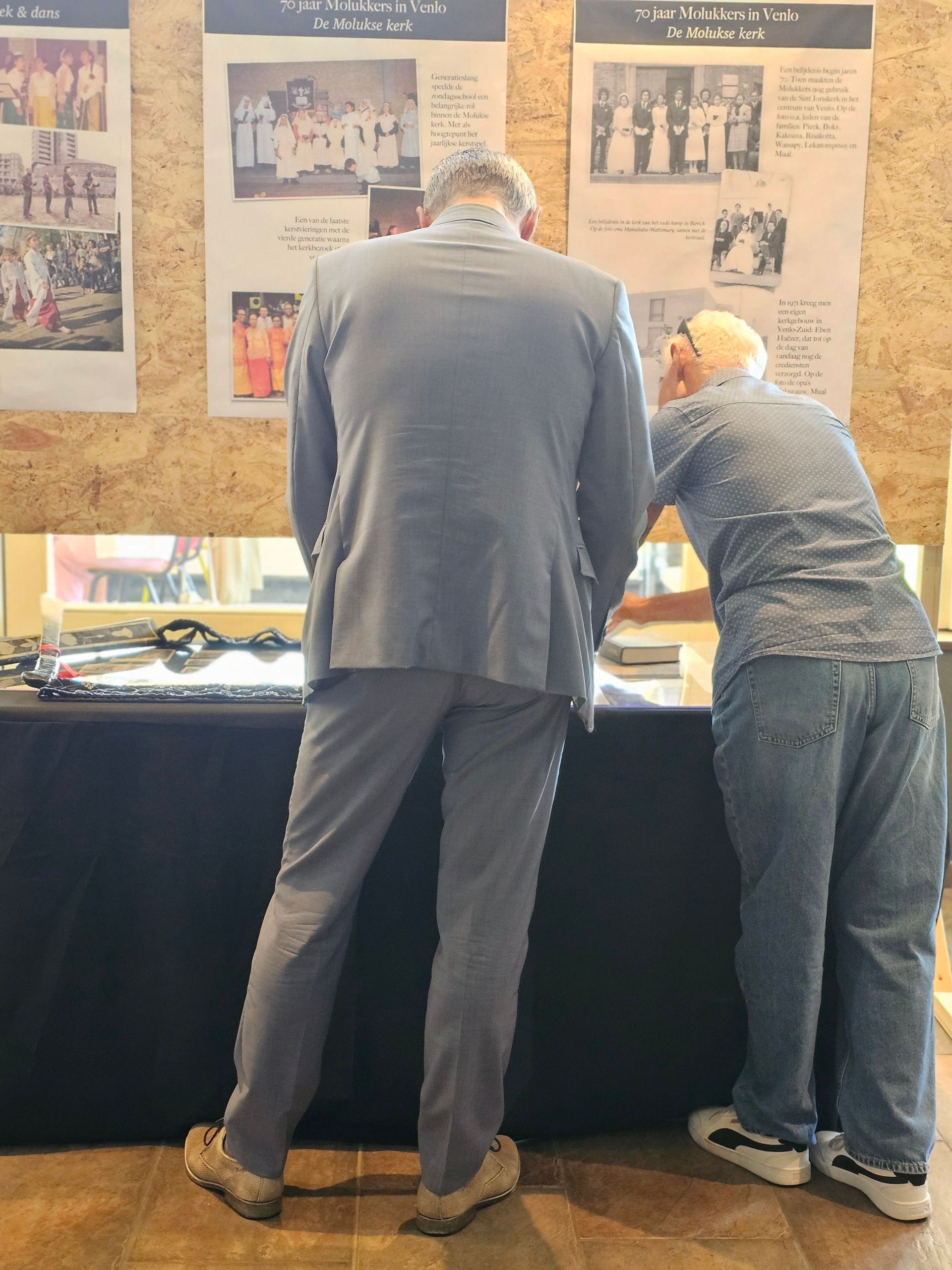 Een man in een pak en een man in een spijkerbroek kijken naar een tafel