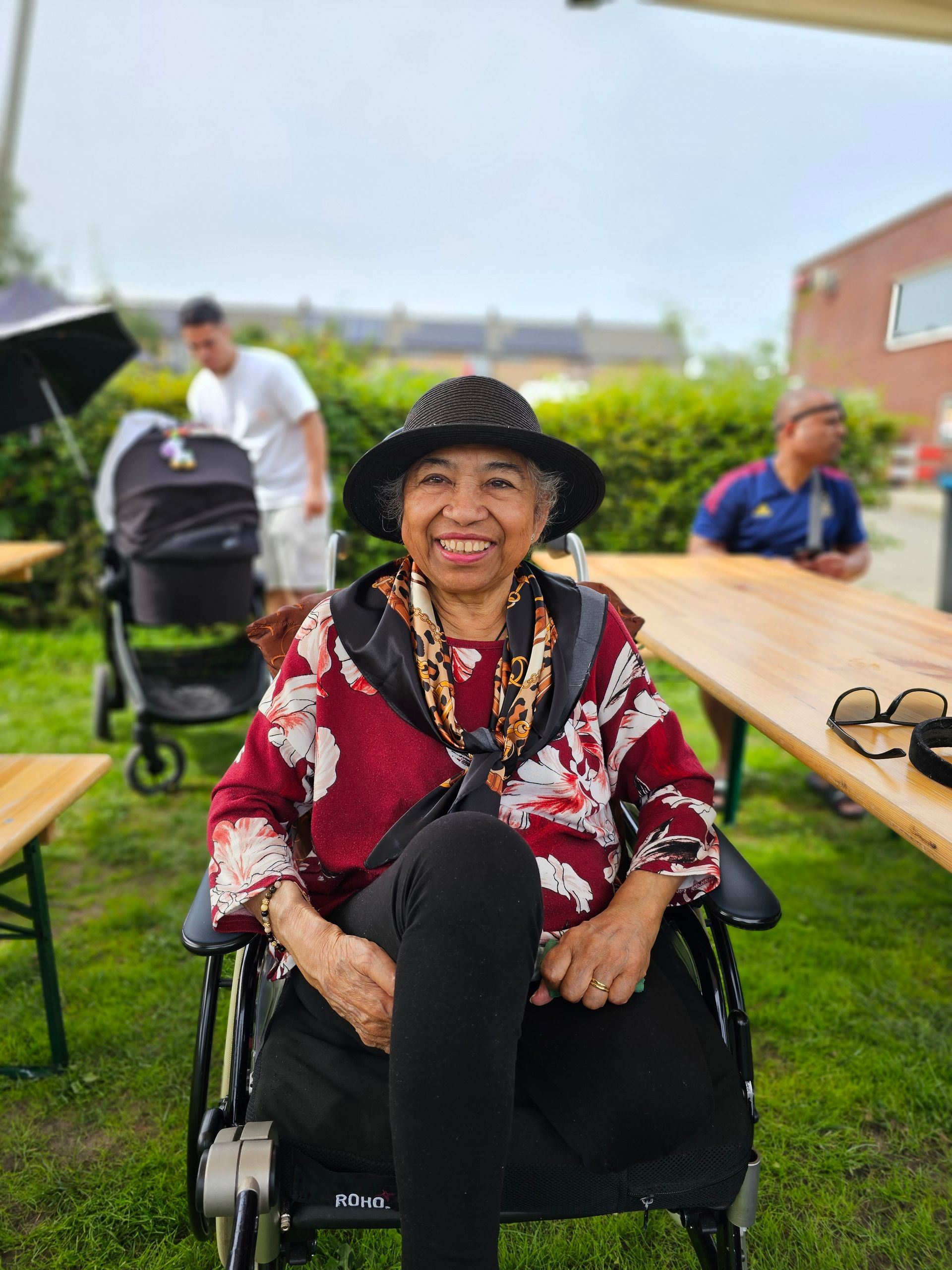 Een oudere vrouw zit in een rolstoel en glimlacht.