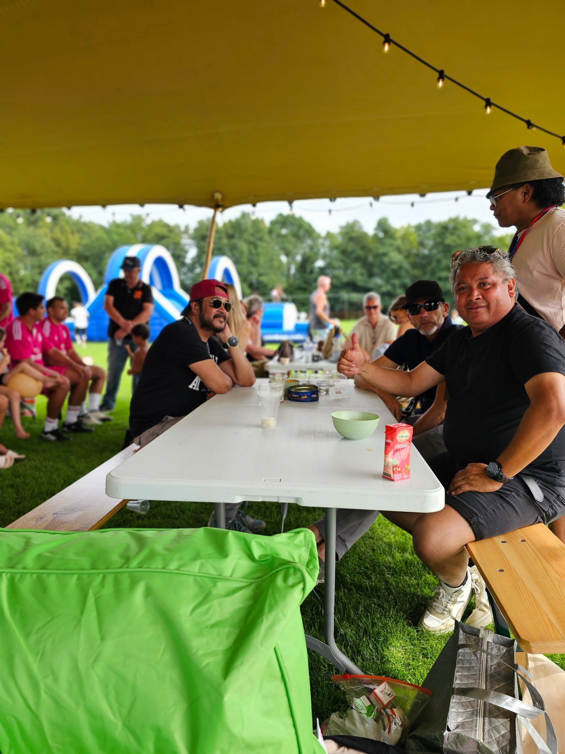Een groep mensen zit aan een lange tafel onder een tent.