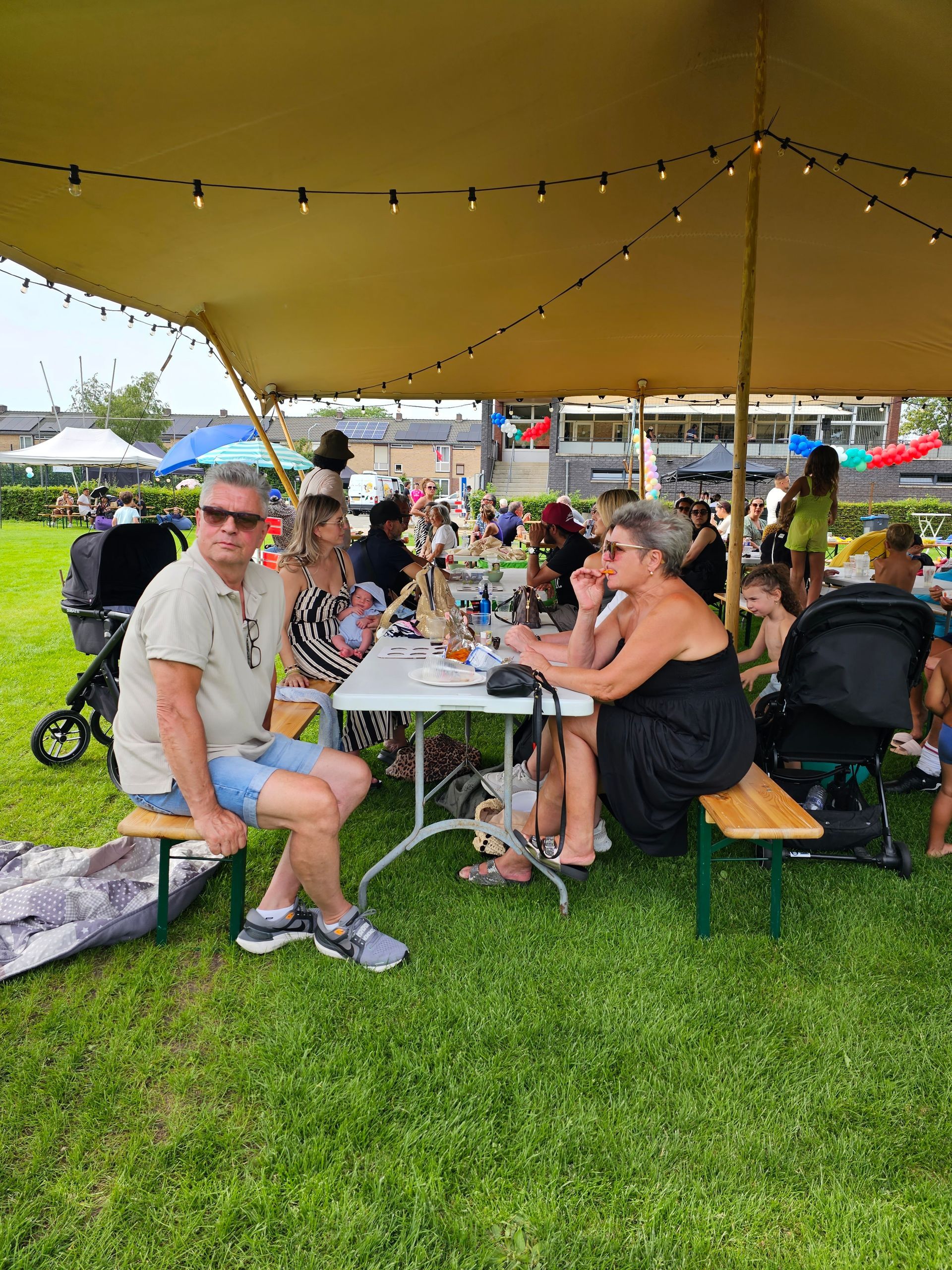 Een groep mensen zit aan een tafel onder een tent.