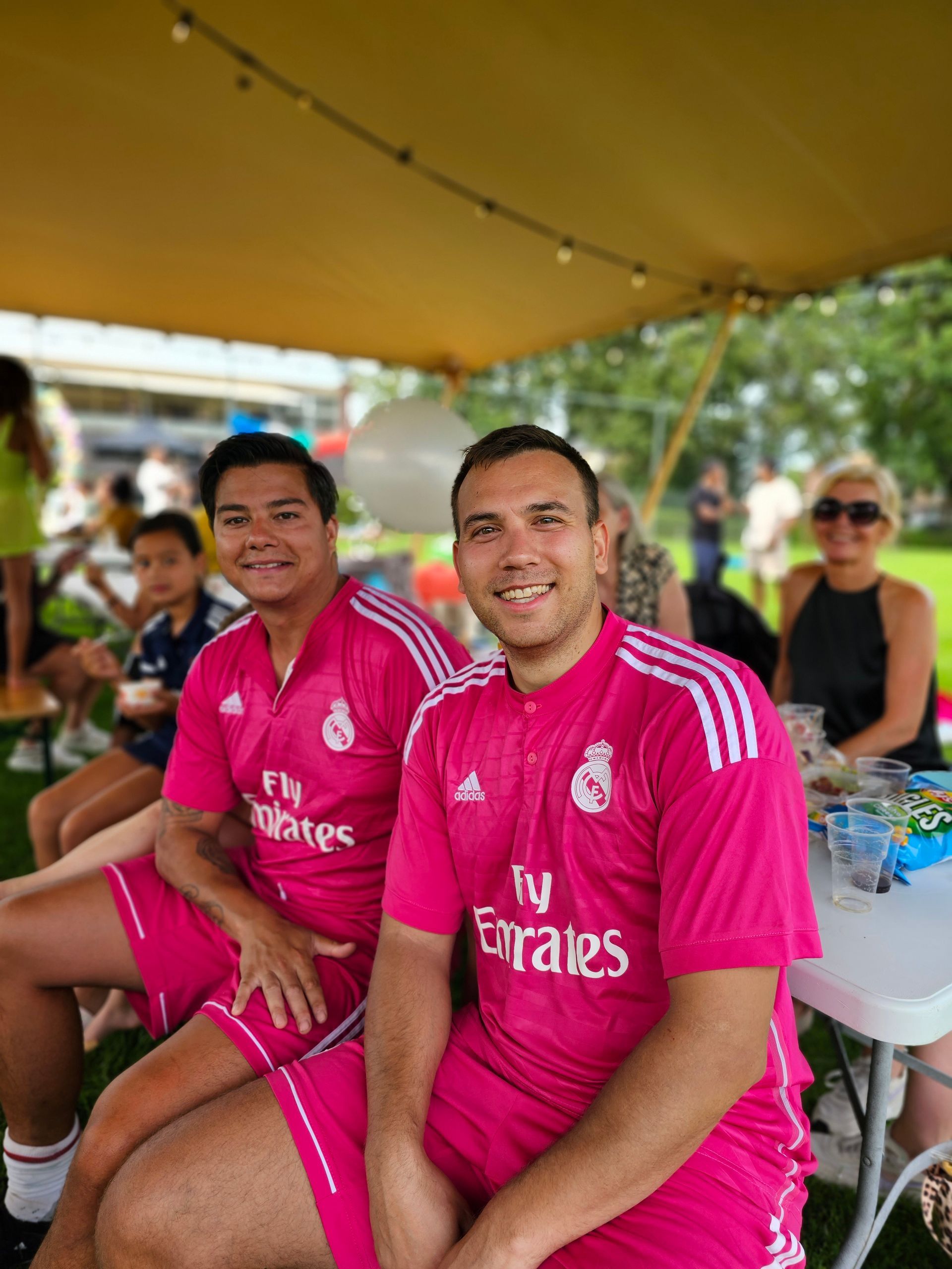 Twee mannen in roze truien van Fly Emirates zitten aan een tafel.