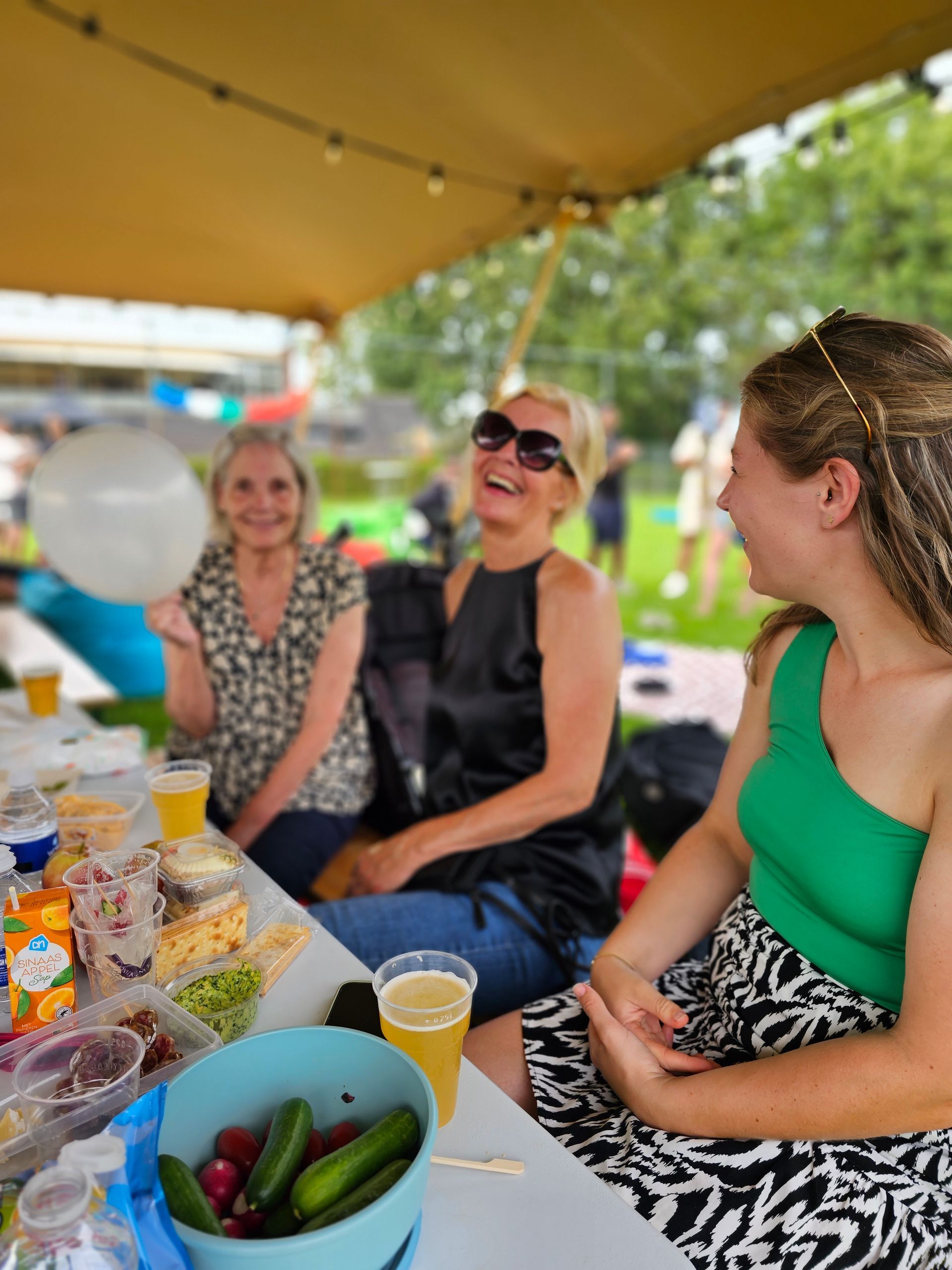 Drie vrouwen zitten aan een tafel met eten en drinken.