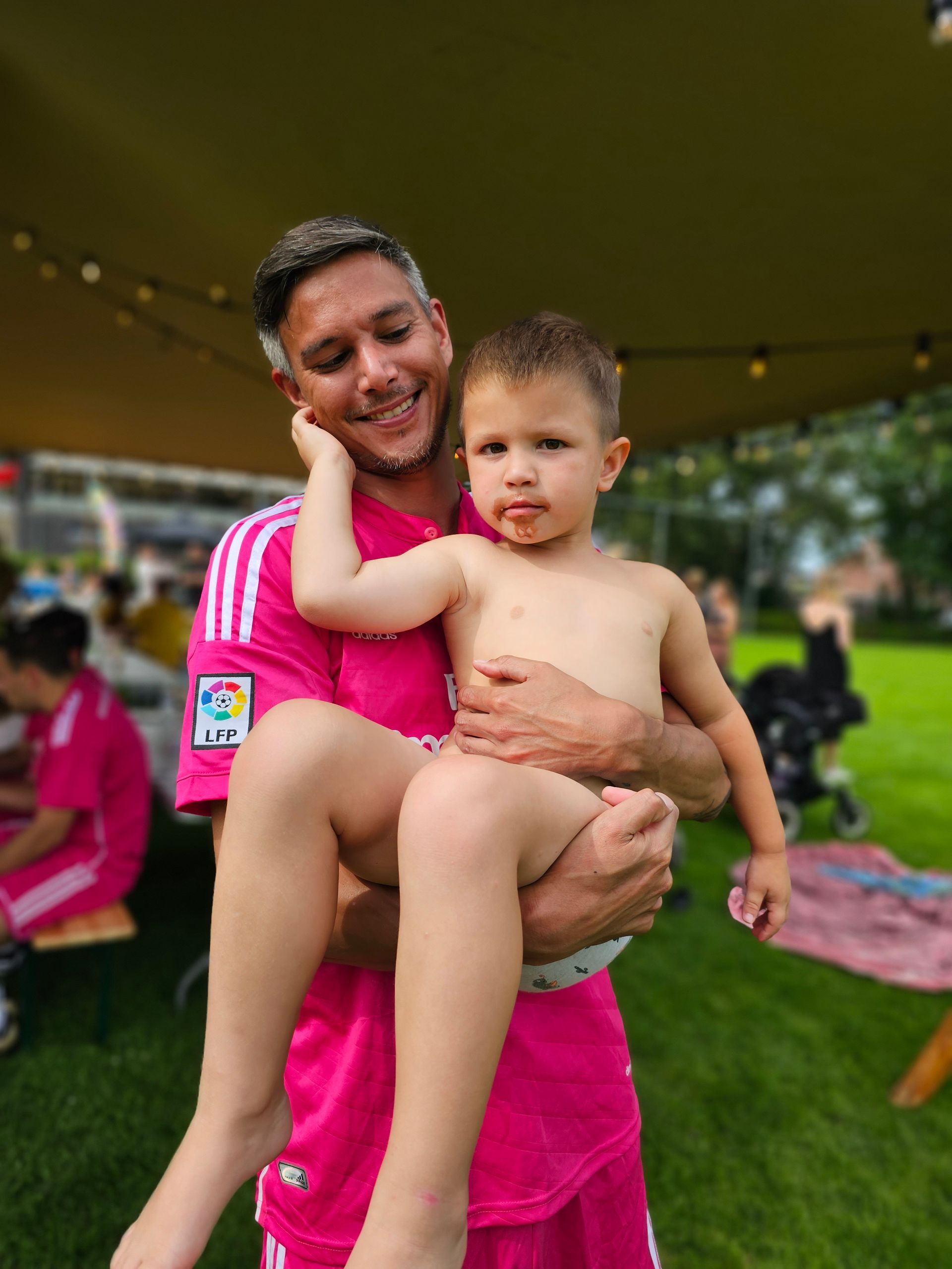 Een man in een roze shirt houdt een baby in zijn armen.