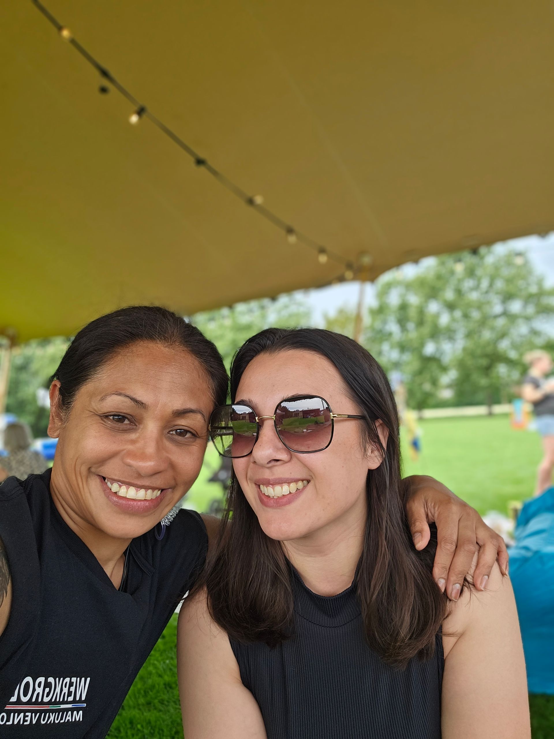 Twee vrouwen met een zonnebril poseren voor een foto onder een tent.
