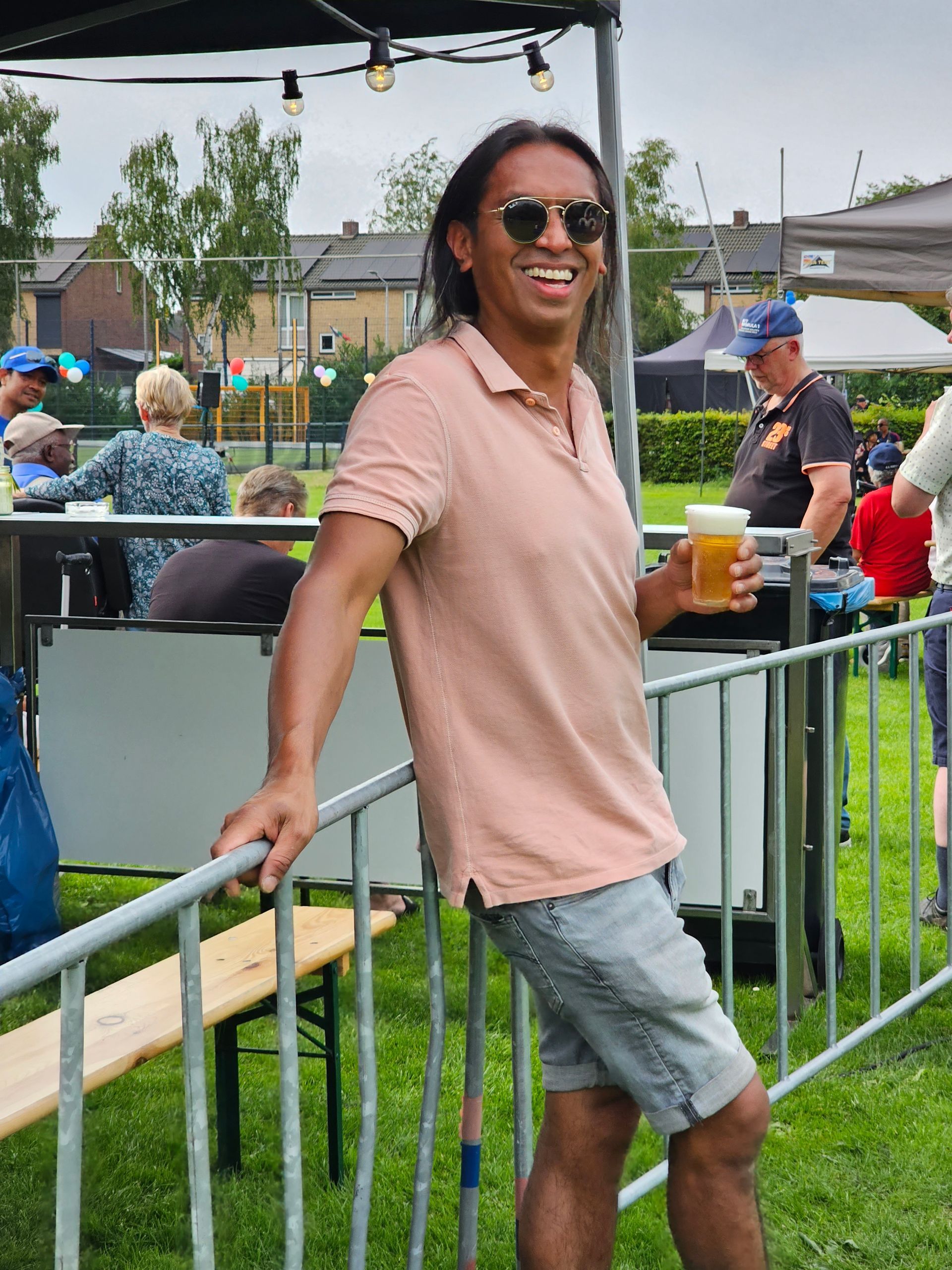 Een man leunend op een hek met een glas bier in zijn hand