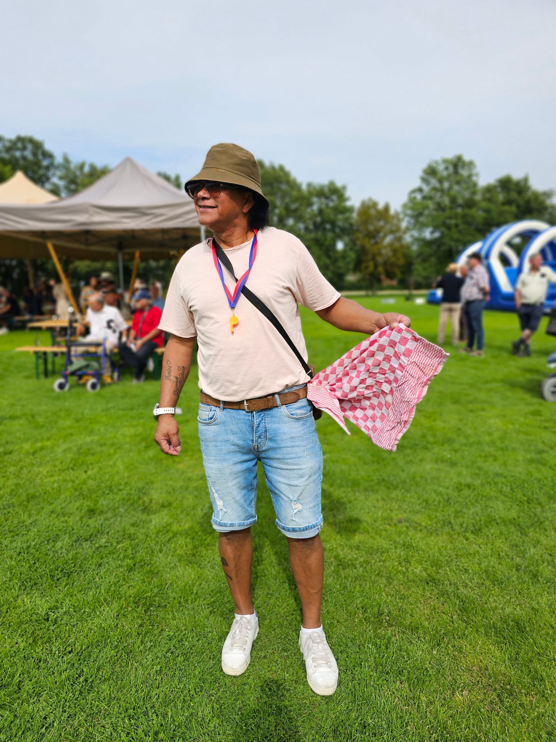 Een man met een hoed en een korte broek staat in een grasveld met een sjaal in zijn hand.
