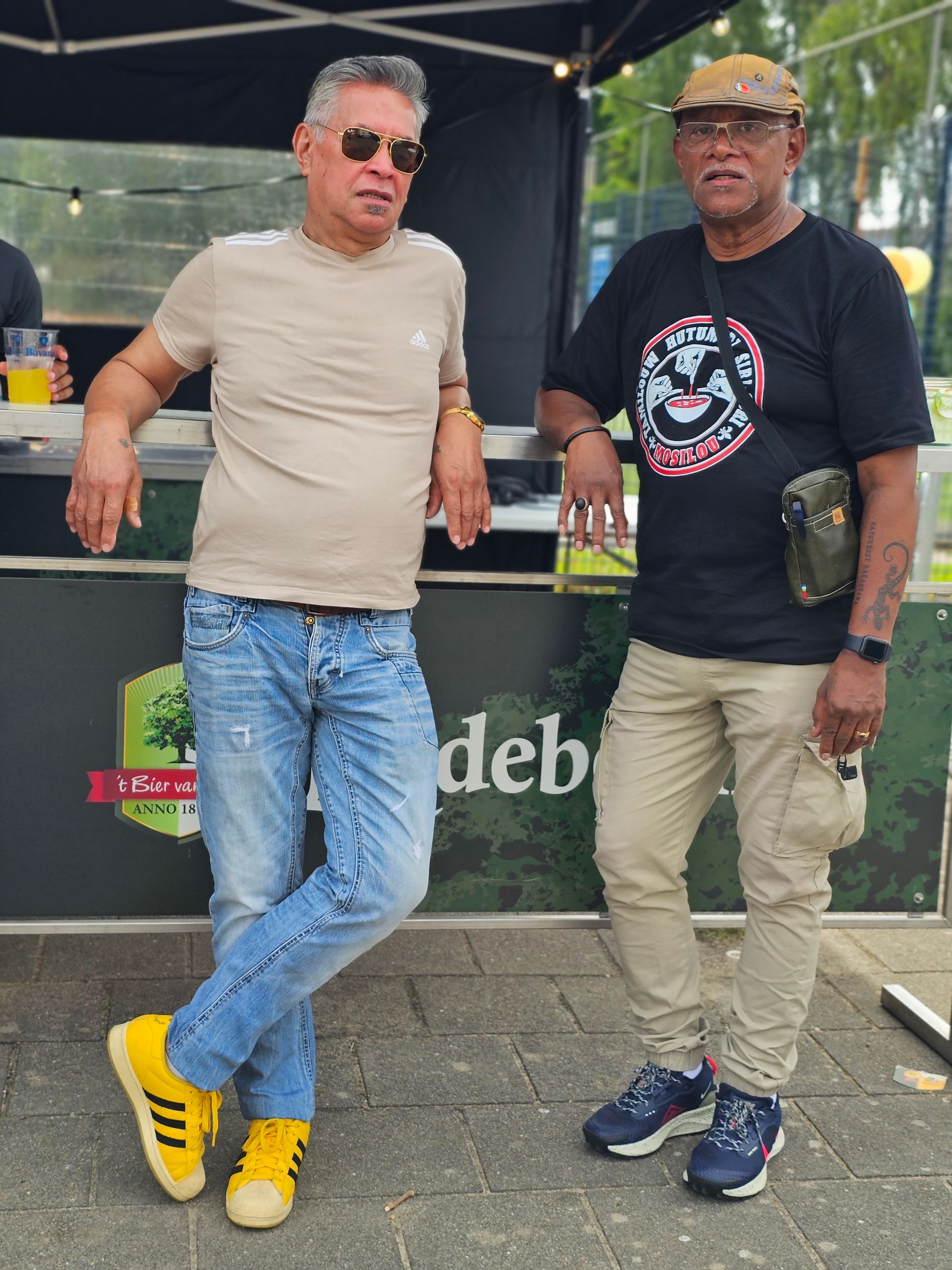 Voor een tent staan ​​twee mannen naast elkaar.