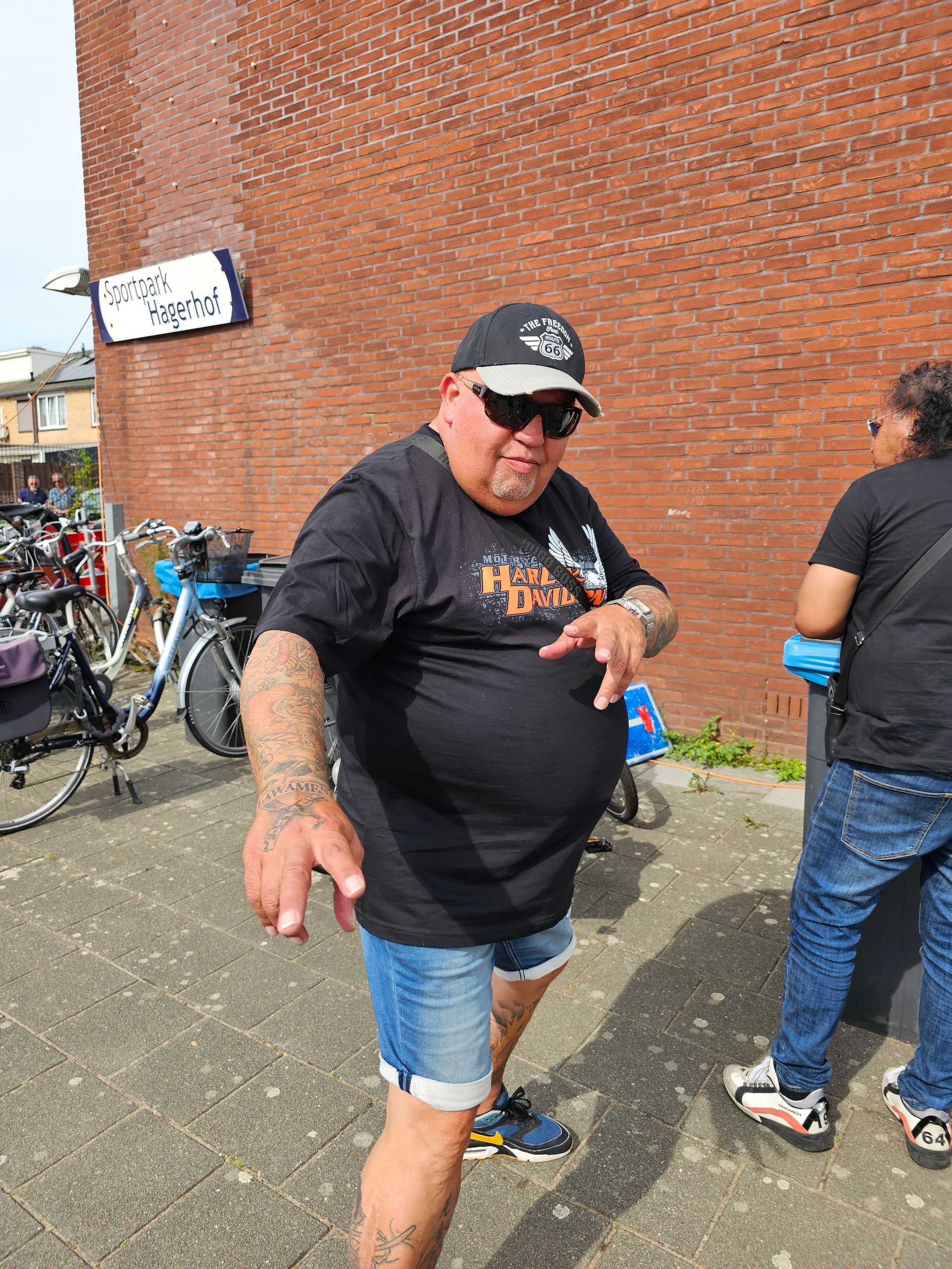 Een man met een hoed en een zonnebril staat voor een bakstenen muur.