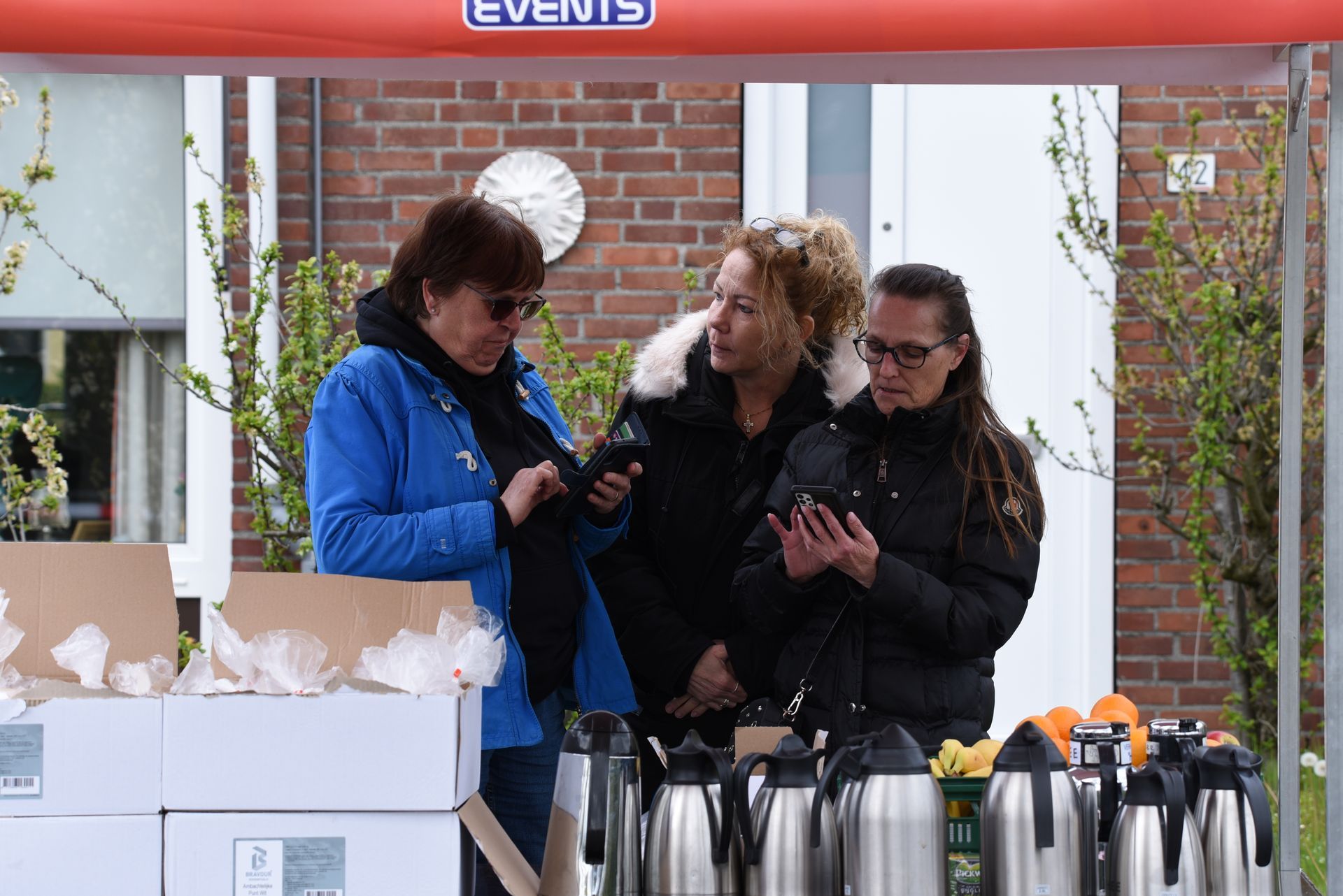 Drie vrouwen staan ​​onder een tent en kijken naar hun telefoons.