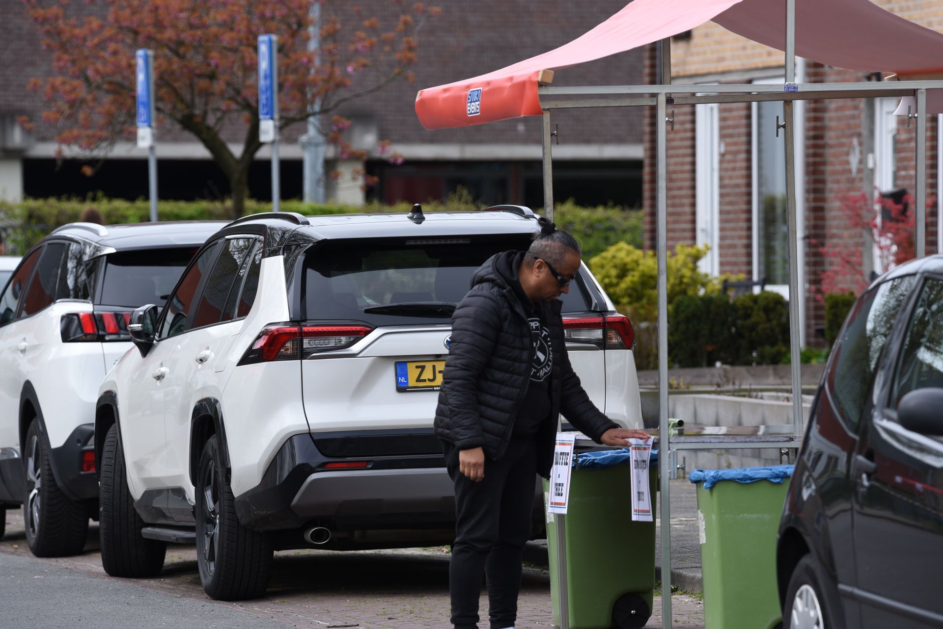 Een man staat naast een vuilnisbak op een parkeerplaats.