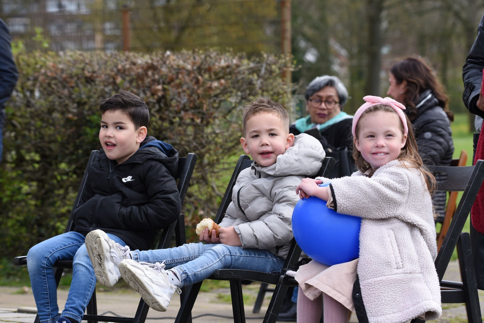 Een groep kinderen zit op stoelen in een park.