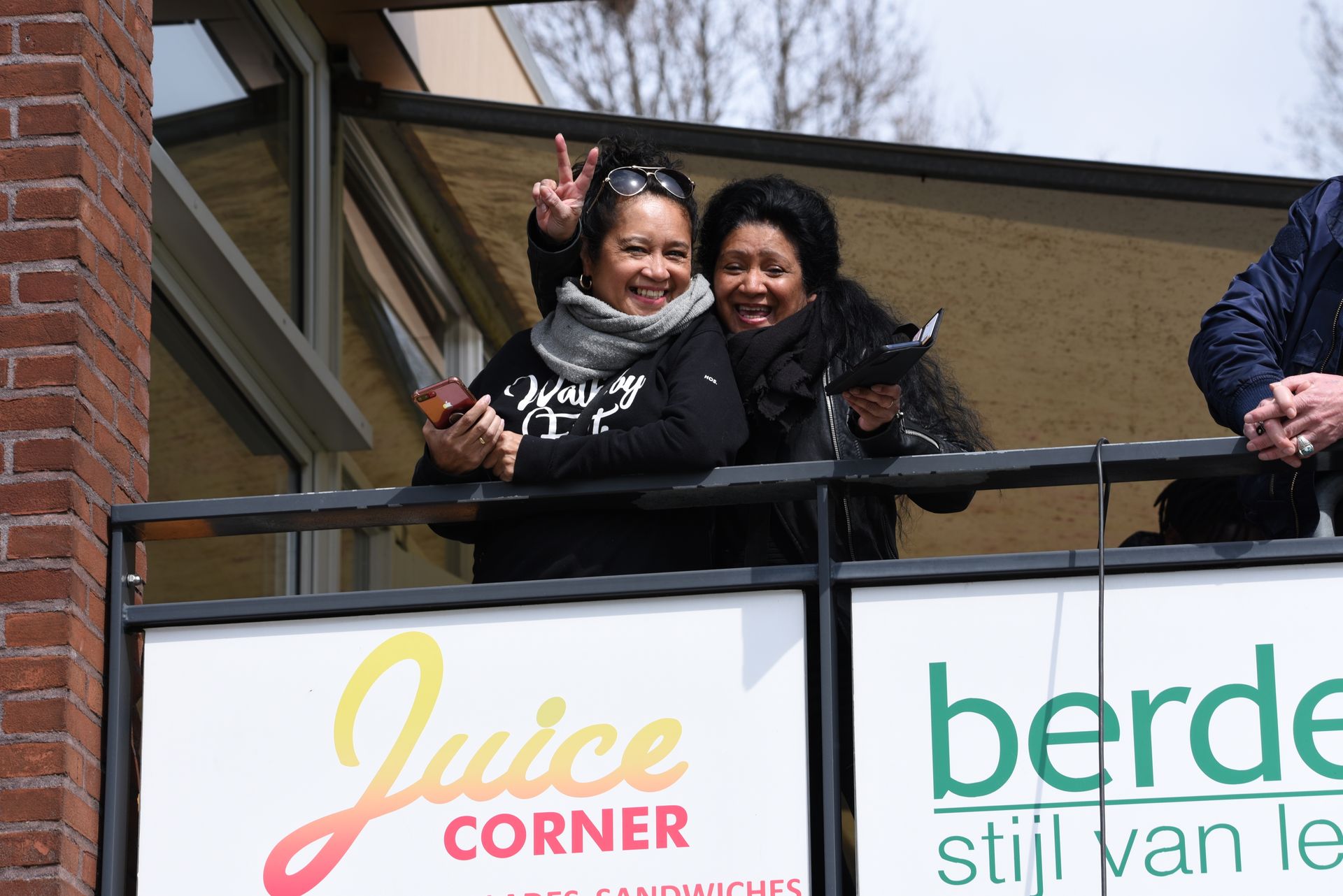 Twee vrouwen staan ​​op een balkon voor een bord met een saphoek.
