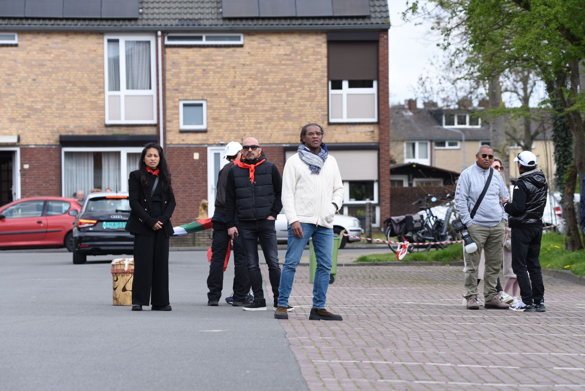 Een groep mensen staat op een parkeerplaats voor een bakstenen gebouw.