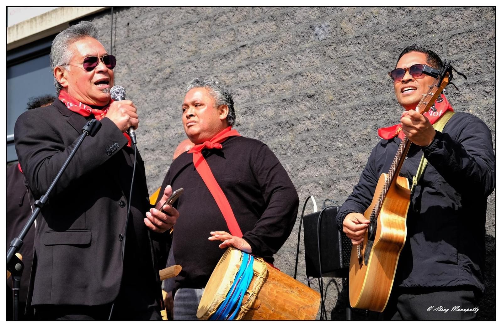 Drie mannen zingen en spelen gitaar voor een microfoon.