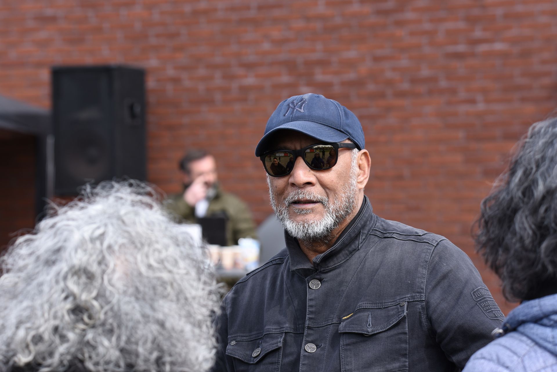 Een man met een zonnebril en een hoed praat met een groep mensen.