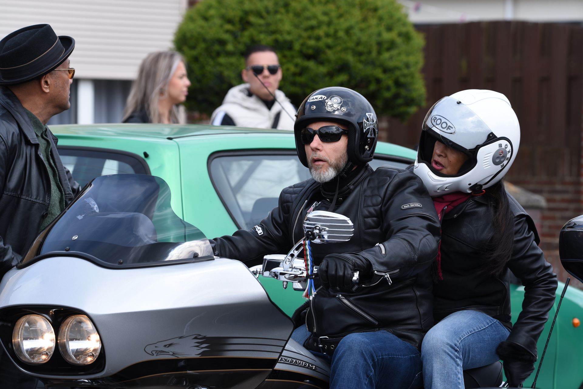 Een man en een vrouw rijden op een motorfiets naast een groene auto.
