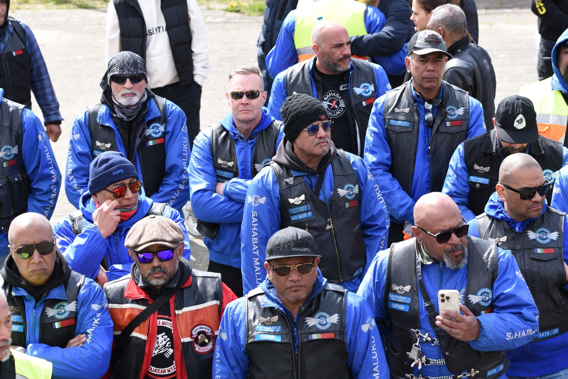 Een groep mannen, gekleed in blauwe jassen en leren vesten, staat in een rij.