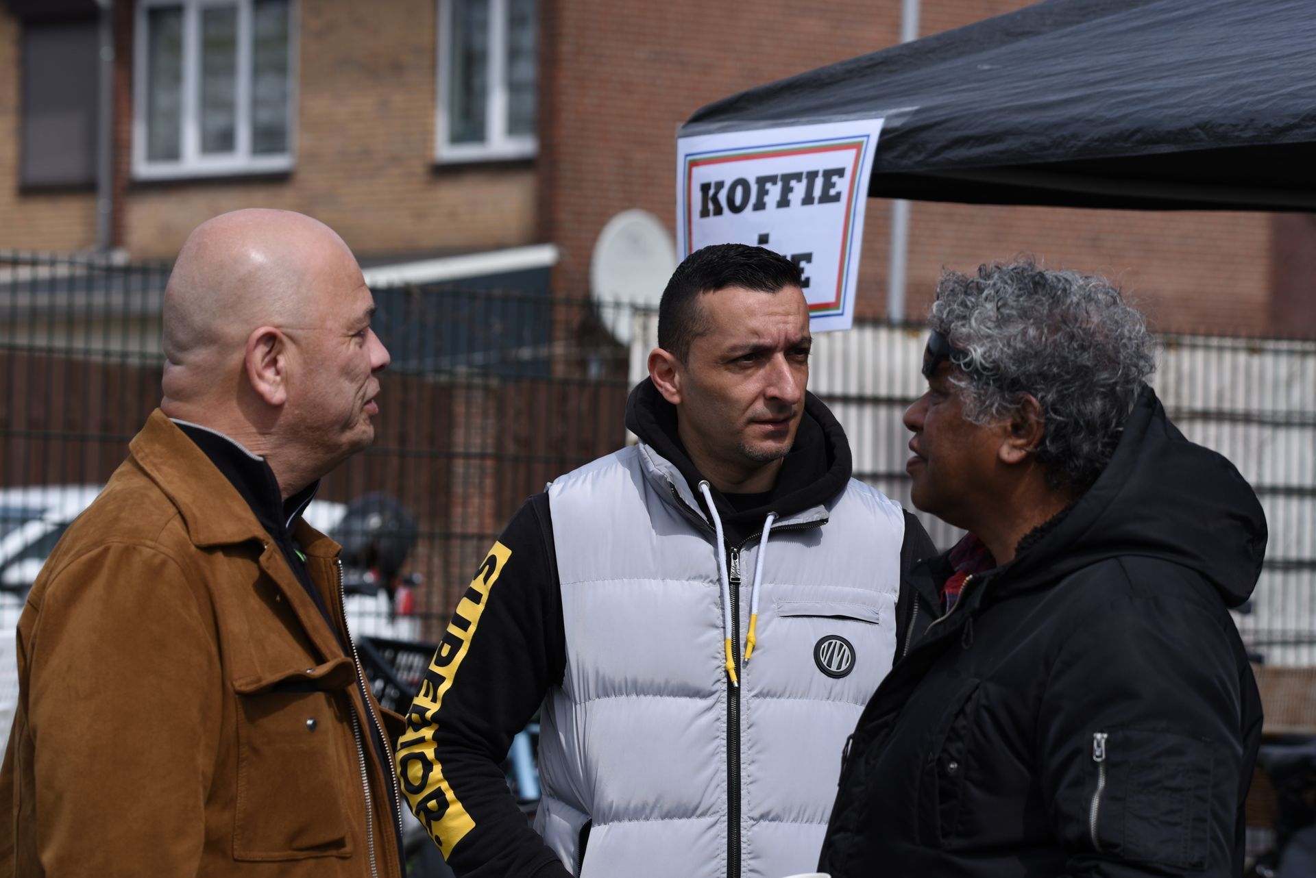 Een groep mensen staat onder een tent met elkaar te praten.