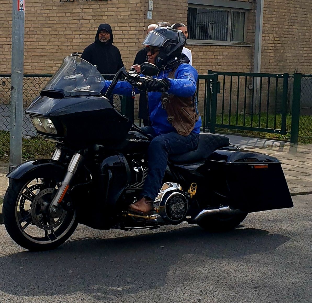 Een man in een blauw jasje rijdt op een zwarte motorfiets
