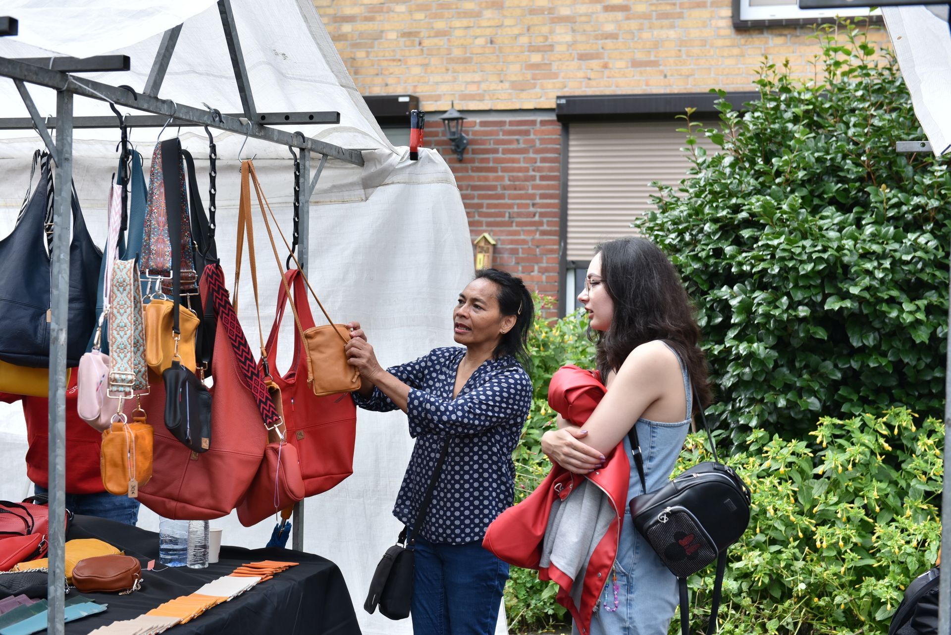 Twee vrouwen kijken naar handtassen op een markt.