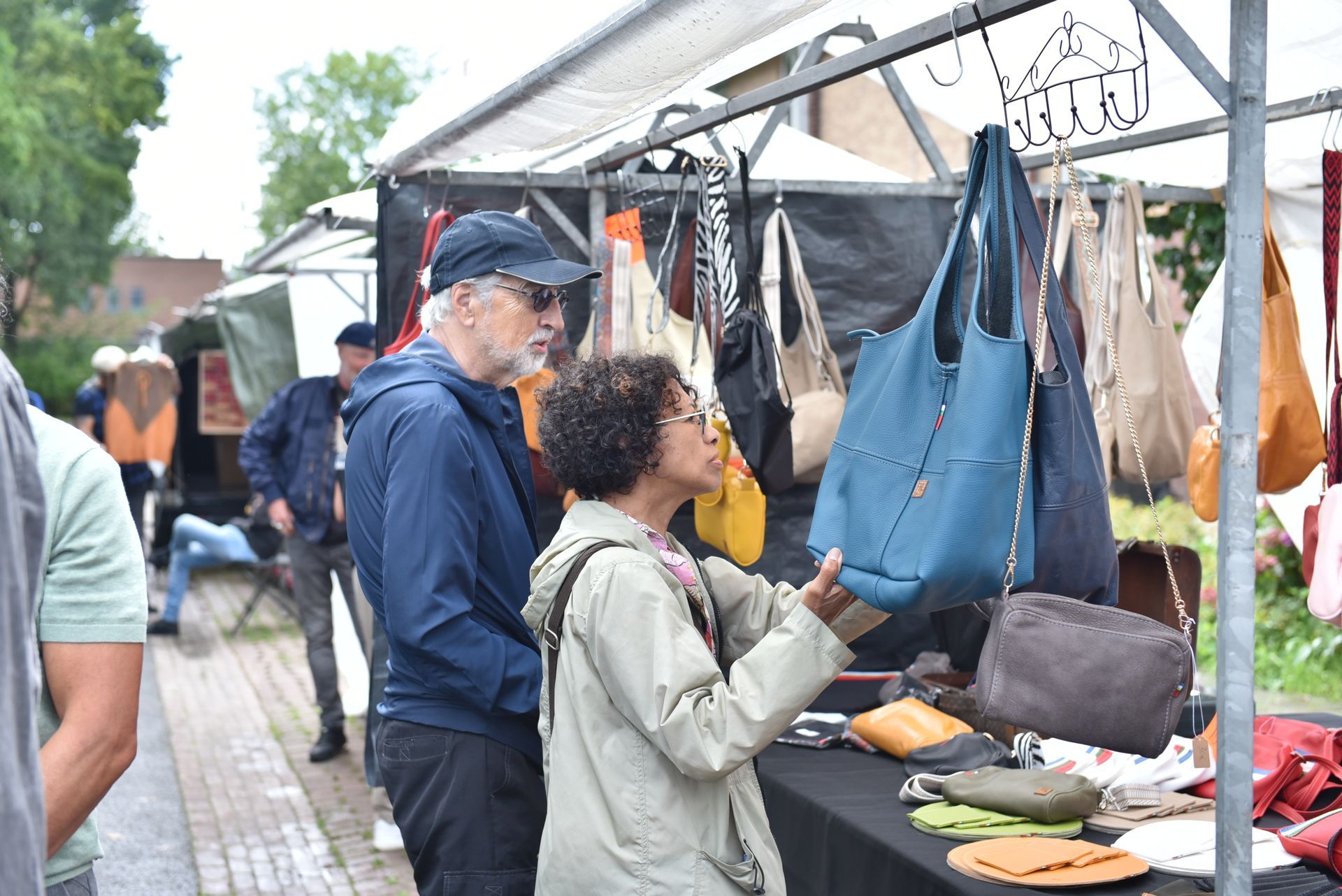 Een man en een vrouw kijken naar handtassen op een markt.