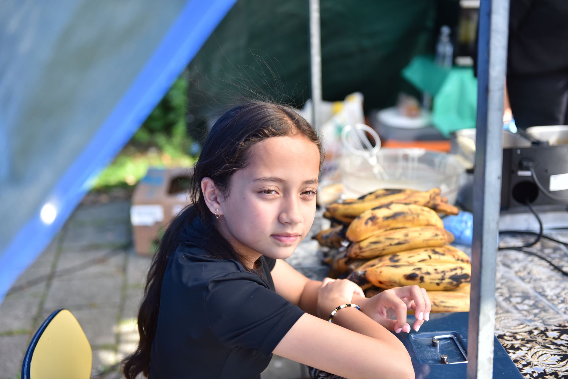Een jong meisje zit aan een tafel met een stapel bananen.