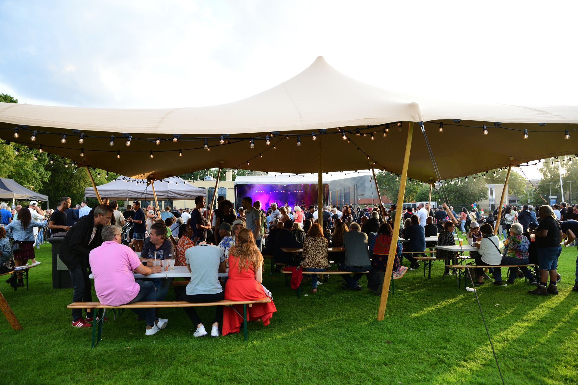 Een groep mensen zit aan tafels onder een tent in een park.