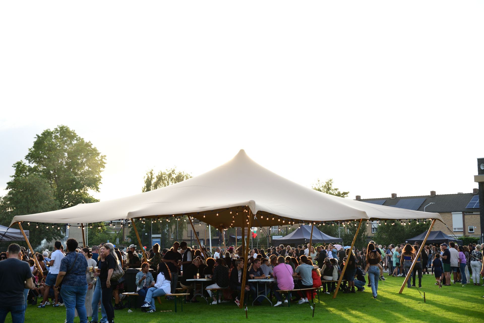 Een grote groep mensen zit onder een tent in een veld.