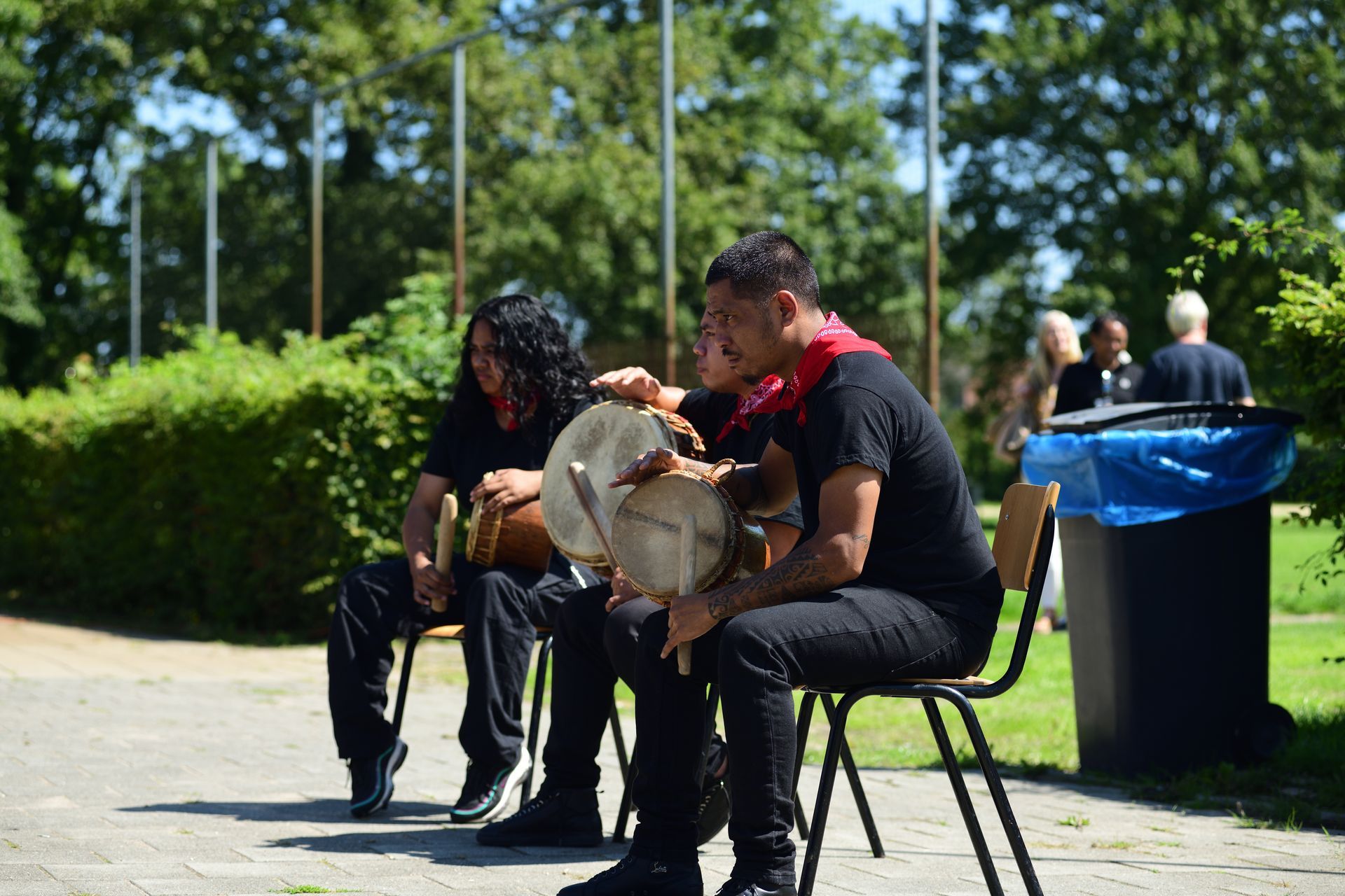 Twee mannen zitten op stoelen in een park en spelen drums.
