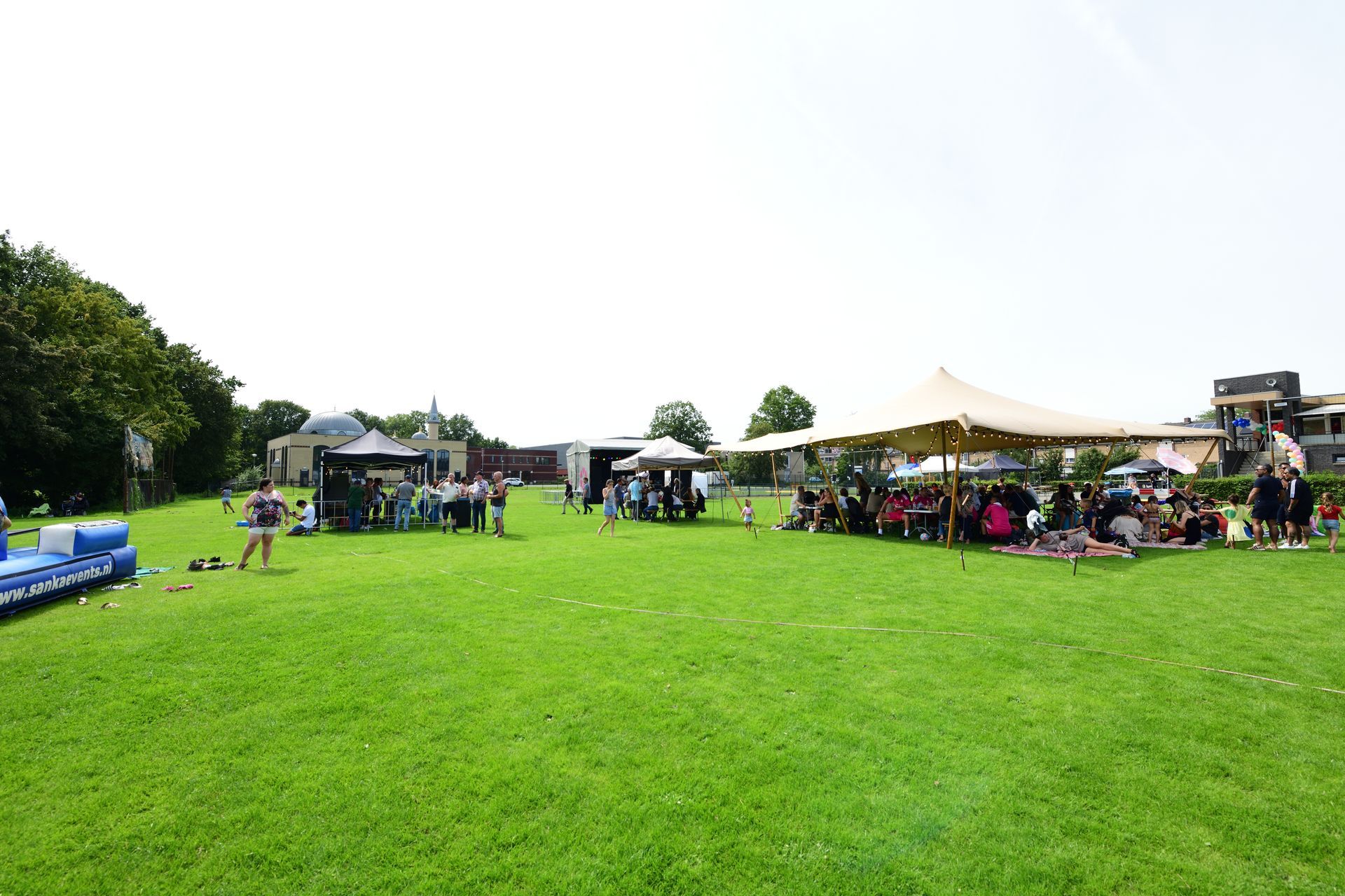 Een groep mensen zit onder tenten in een grasveld.