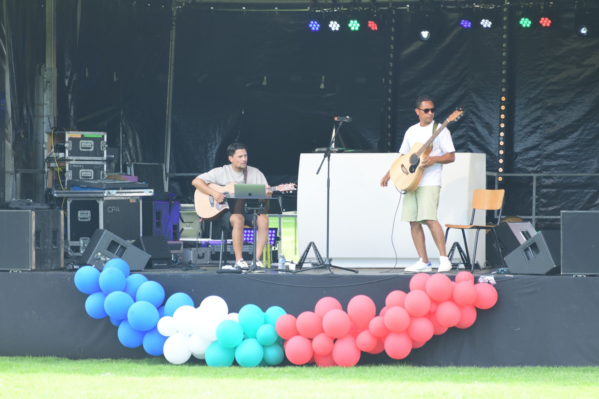 Twee mannen spelen gitaar op een podium met ballonnen op de achtergrond