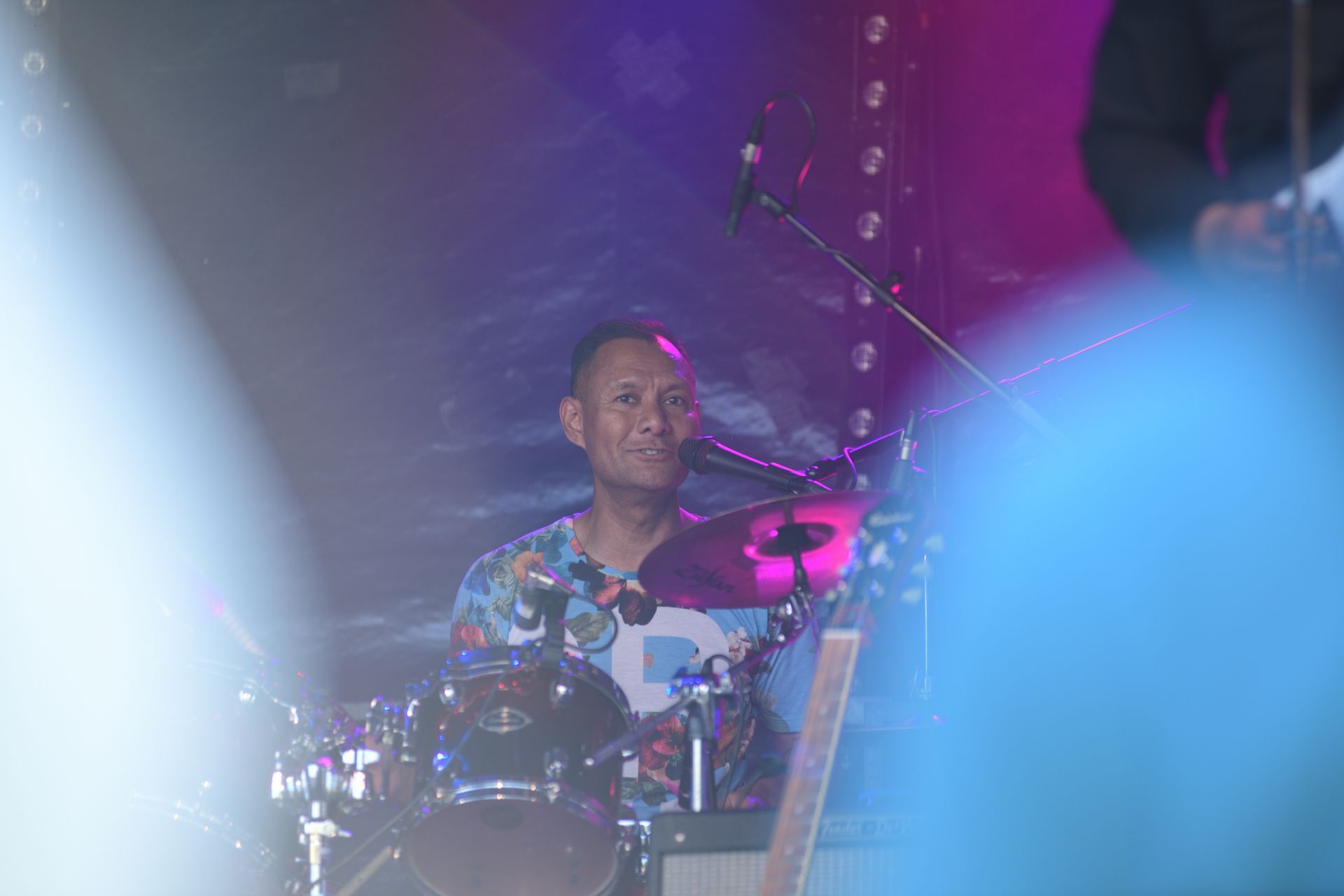 Een man speelt drums op een podium voor een microfoon.