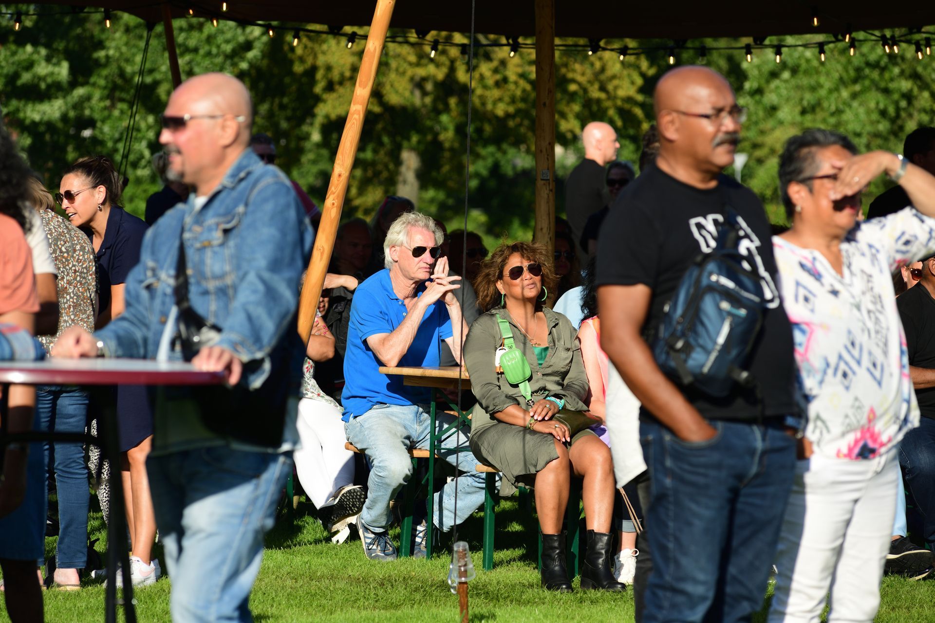 Een groep mensen staat en zit onder een tent.