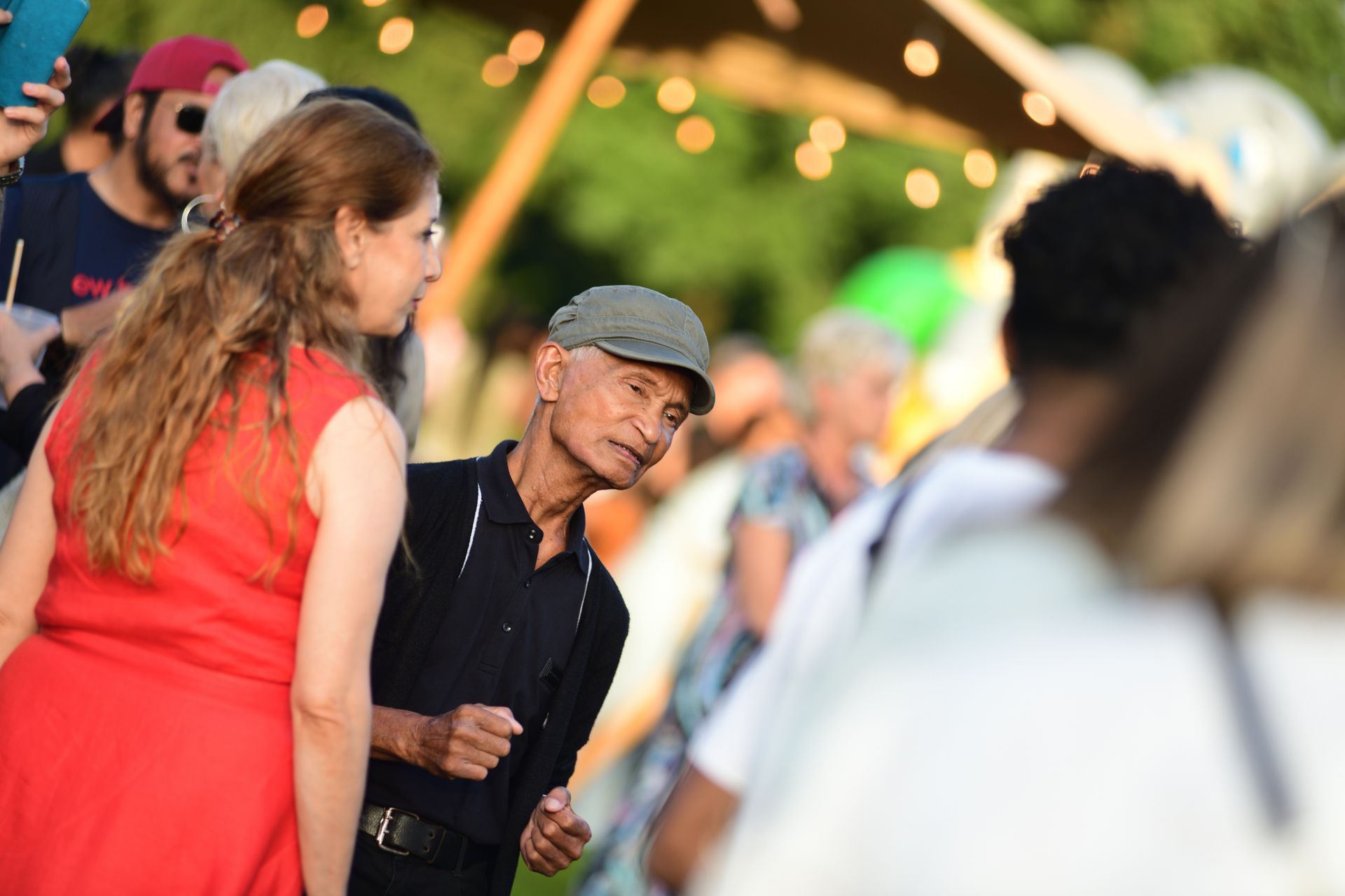 Een man met een hoed praat op een feestje met een vrouw in een rode jurk.