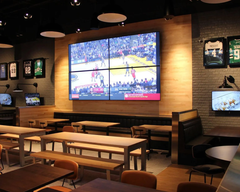 A sports bar interior with multiple TVs showing a basketball game, tables, and booths.