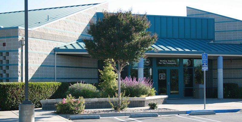Building with turquoise roof and trim, entrance surrounded by landscaping, blue handicap parking sign.