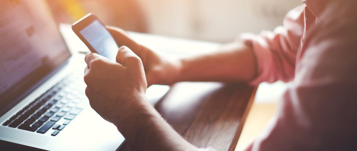 Person holding a smartphone and using a laptop, indoors.