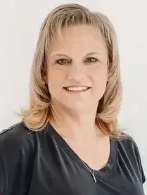 A woman in a red shirt is standing with her arms crossed and smiling.